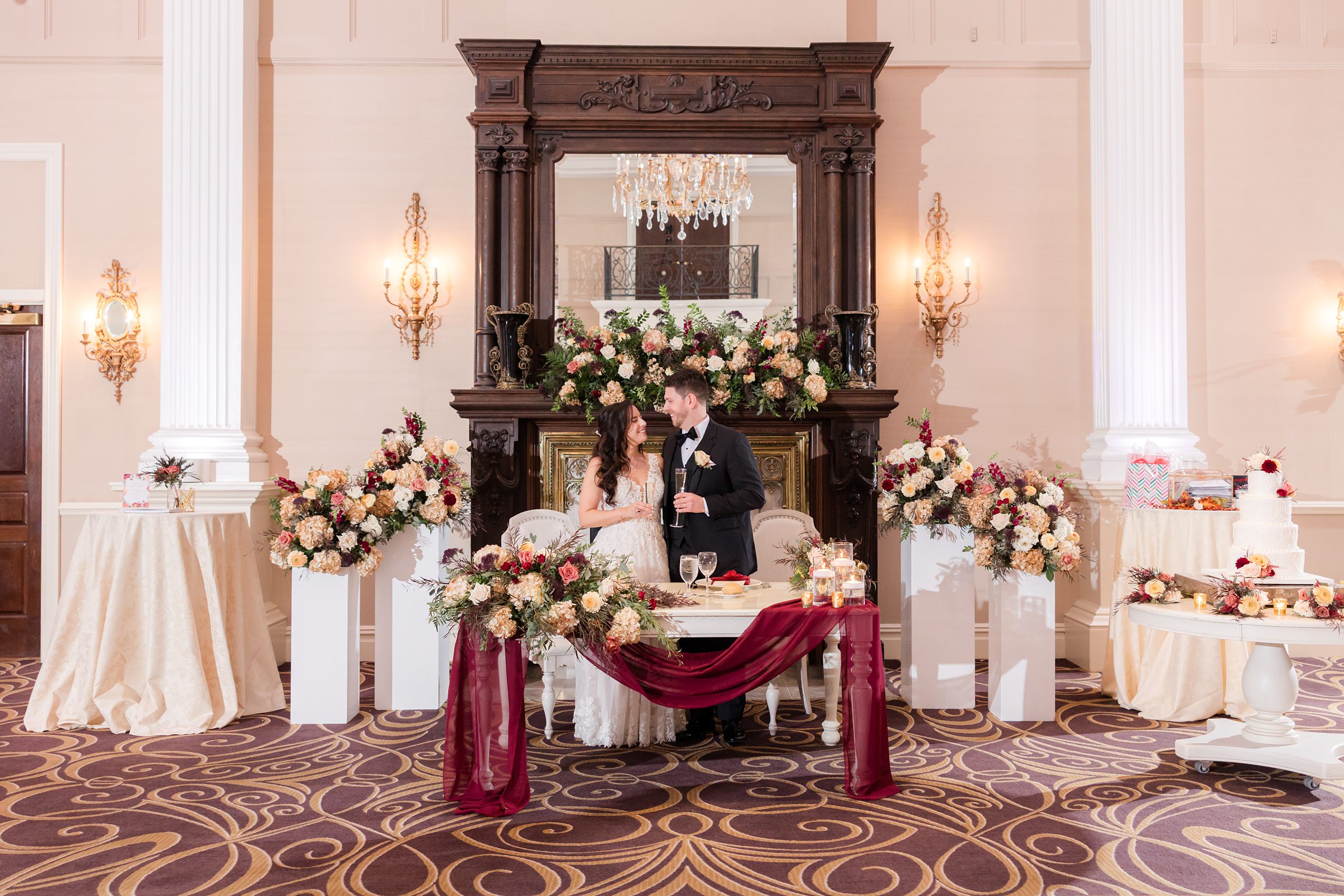 Bride and groom share an intimate moment on a beautifully adorned couch, surrounded by lush florals and soft candlelight, with elegant décor creating a warm, romantic wedding atmosphere