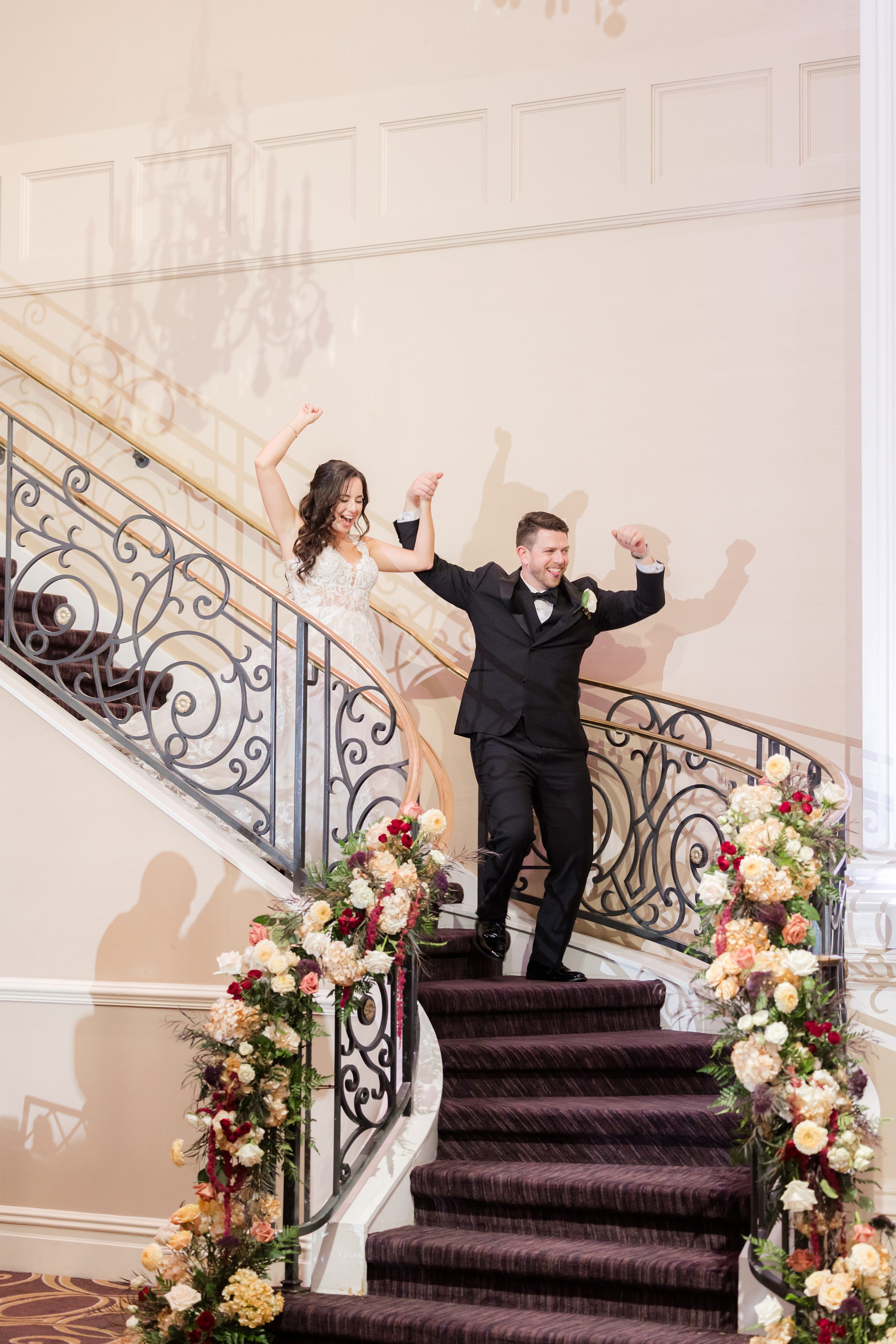 Bride and groom descend an elegant staircase with radiant smiles, celebrating the start of their reception in a moment full of excitement and love