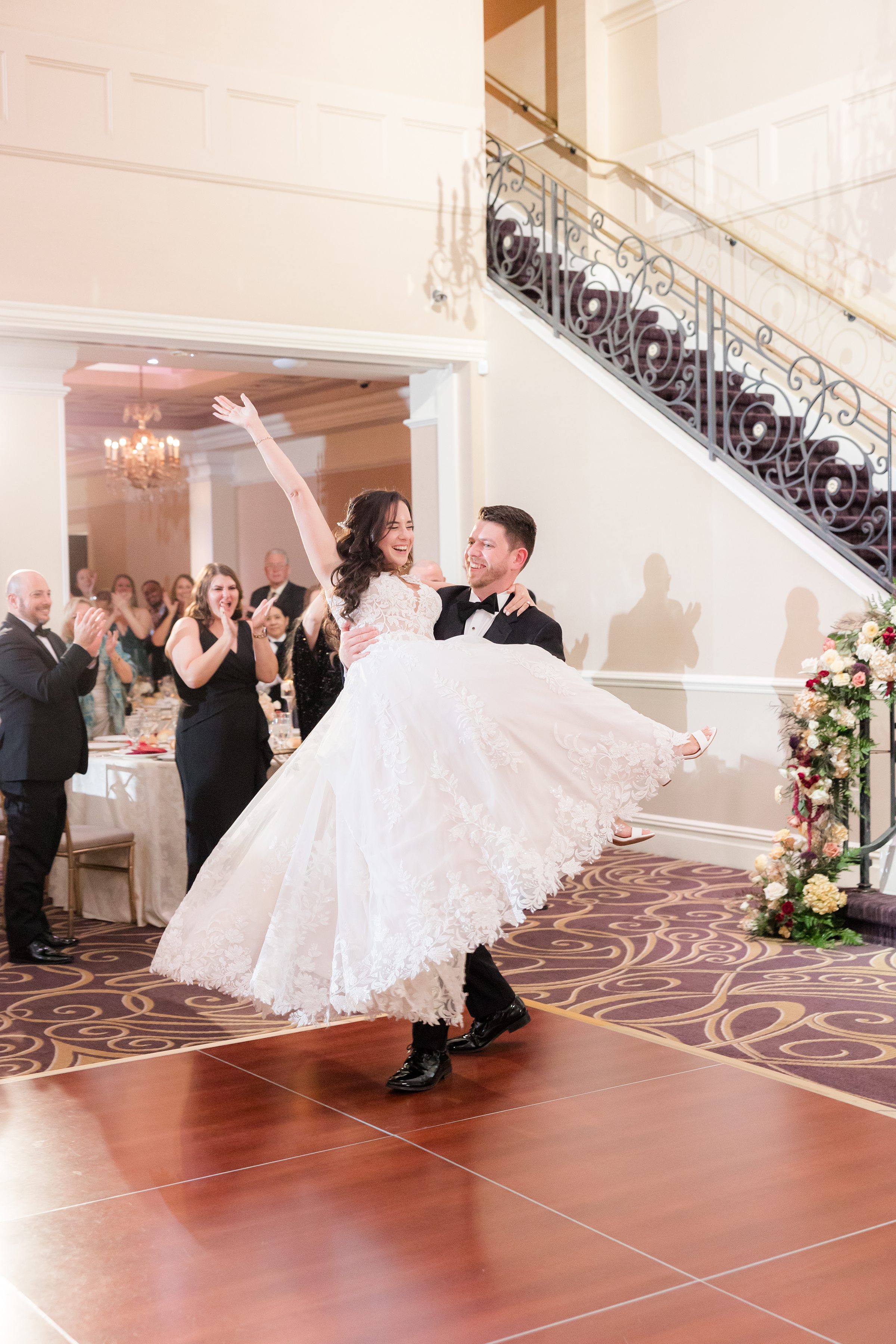Groom carries his bride across the dance floor as guests applaud, marking a joyful and unforgettable entrance