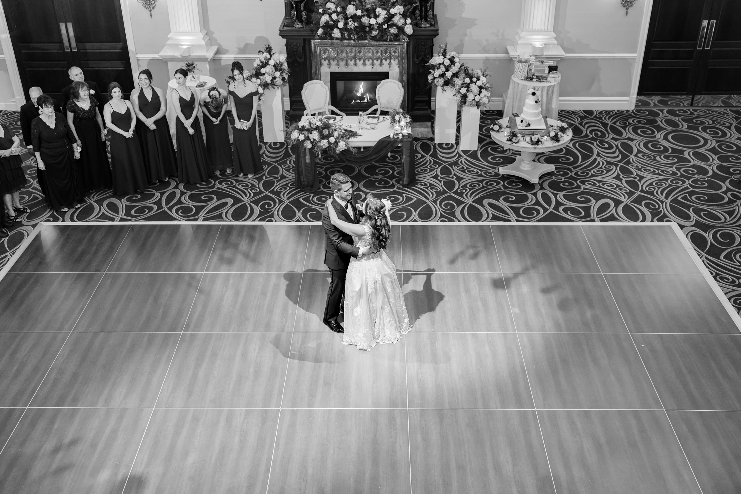 Bride and groom share their first dance at the center of a grand ballroom, holding each other close as guests look on