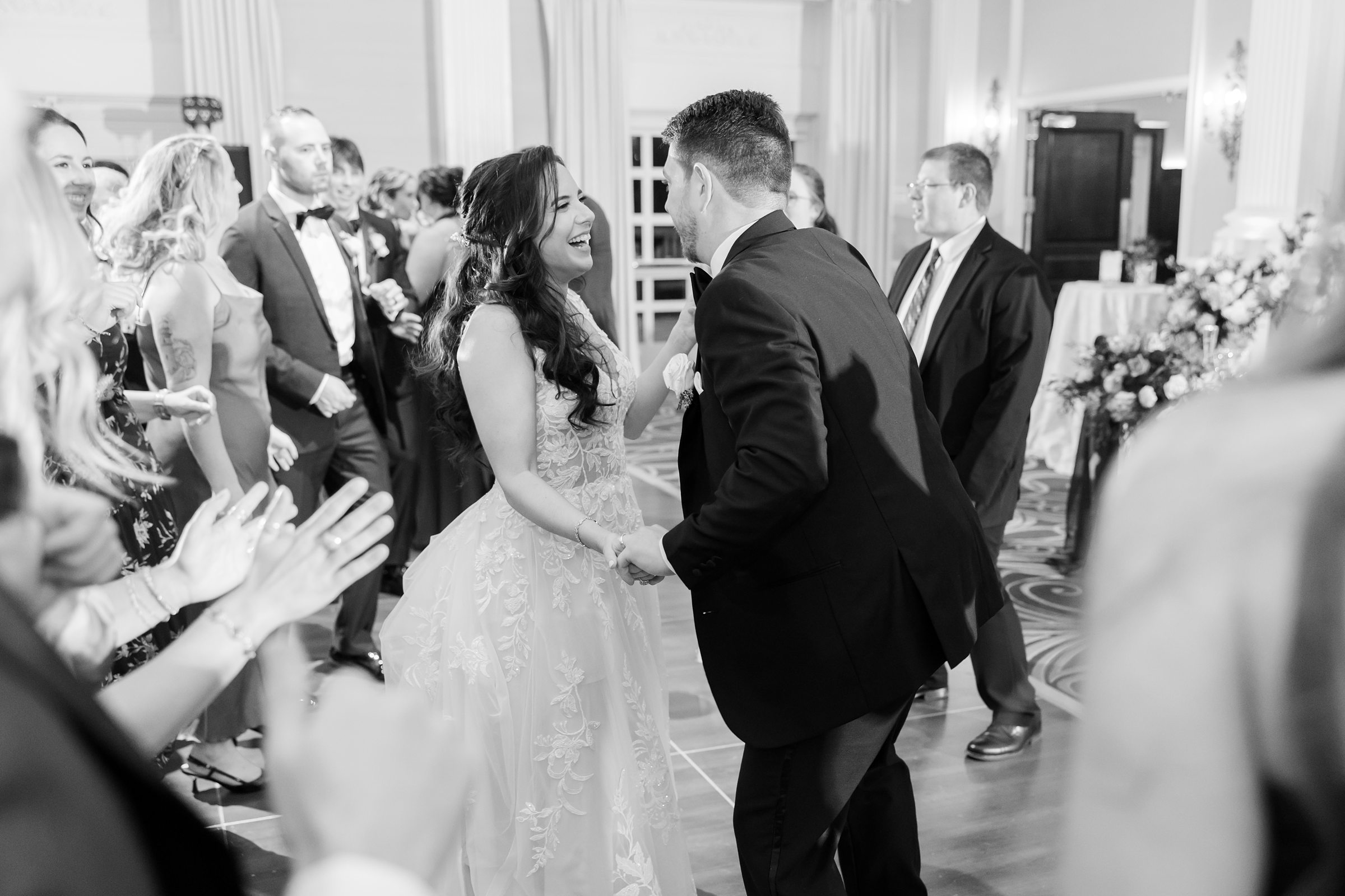 Bride and groom dance together at their reception, smiling and laughing as guests cheer around them