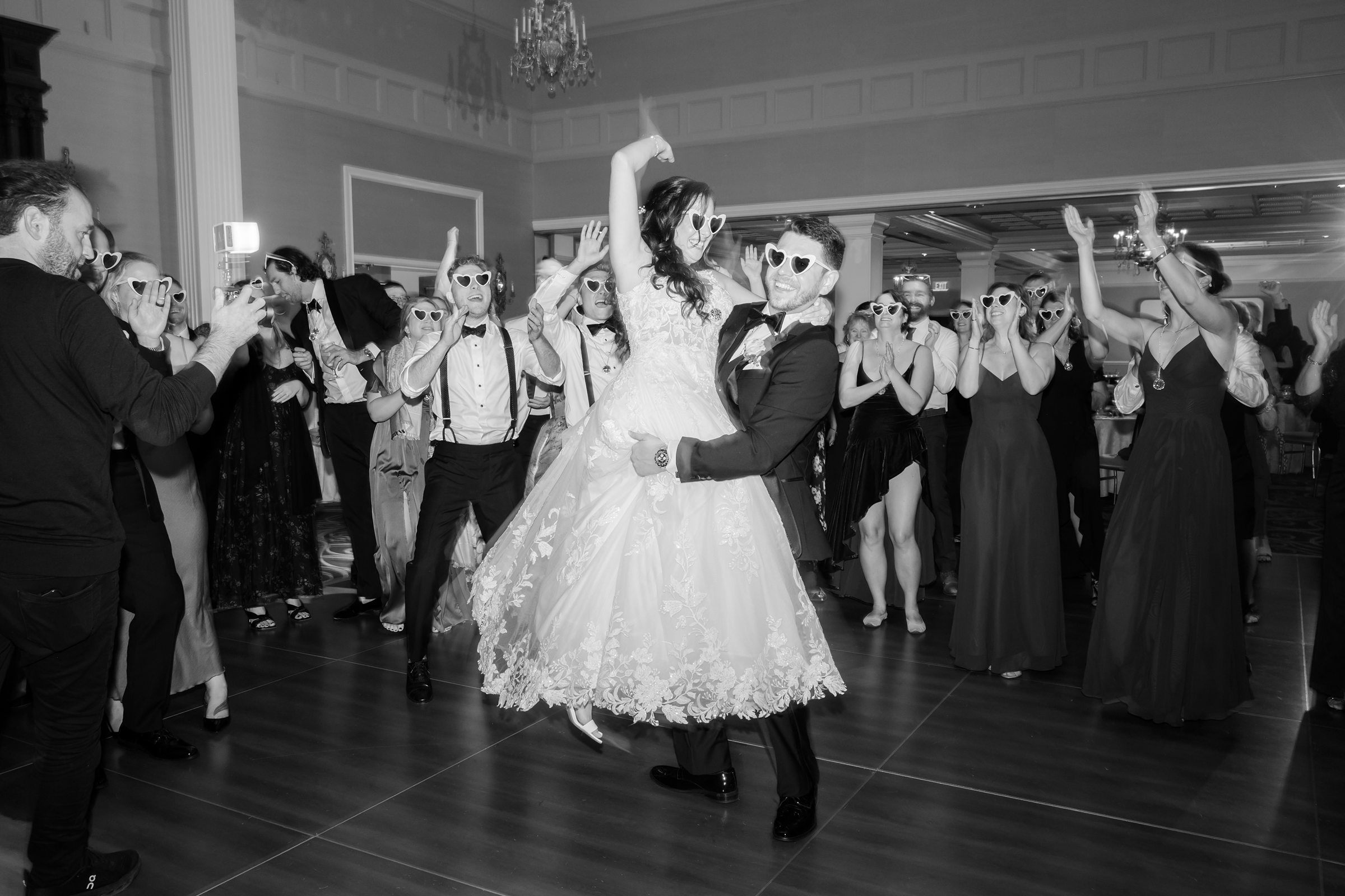 Bride and groom dance at the center of the reception, the groom lifting the bride as guests cheer and celebrate around them