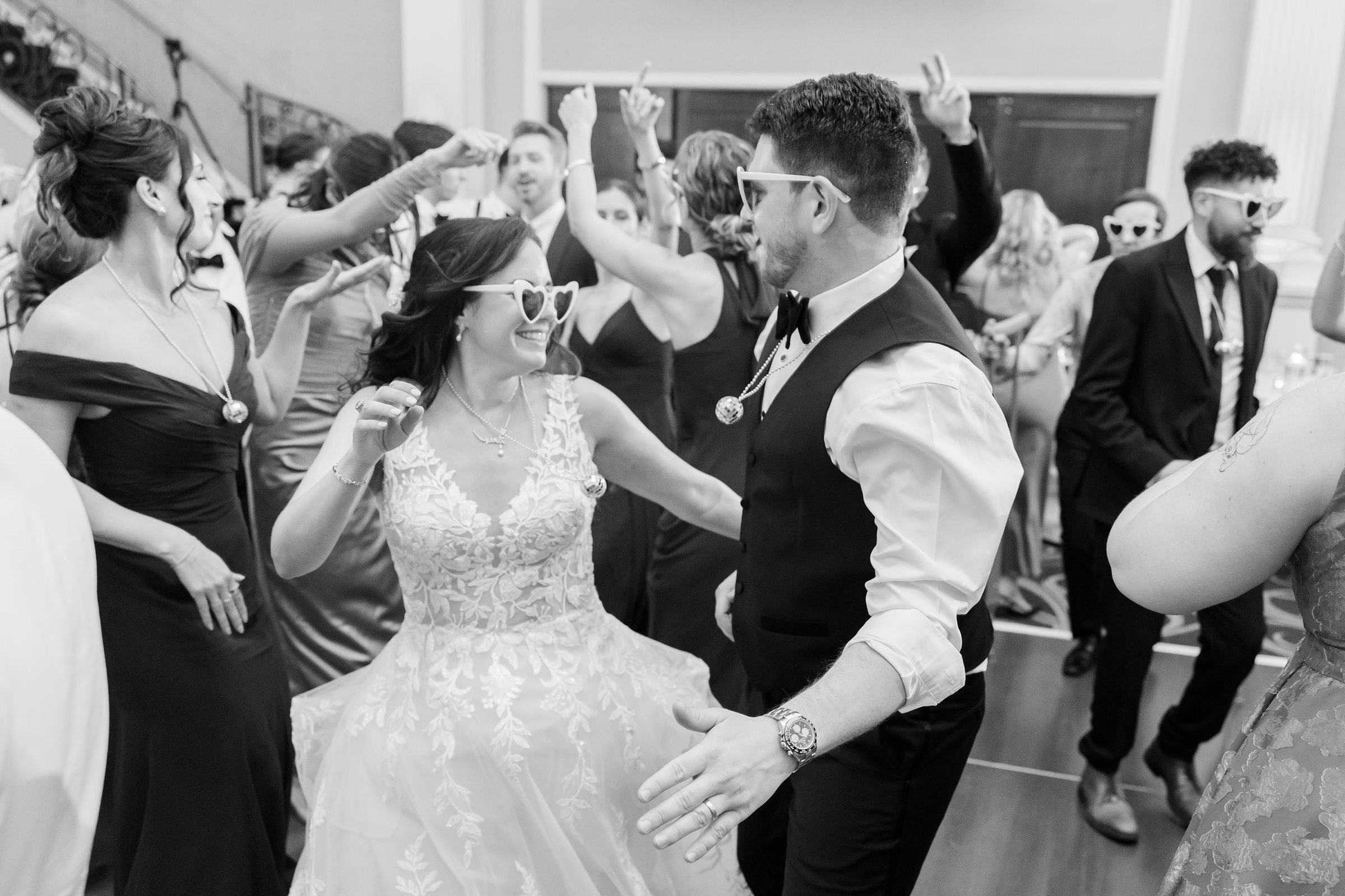 Bride and groom share a fun, energetic dance surrounded by cheering friends and family