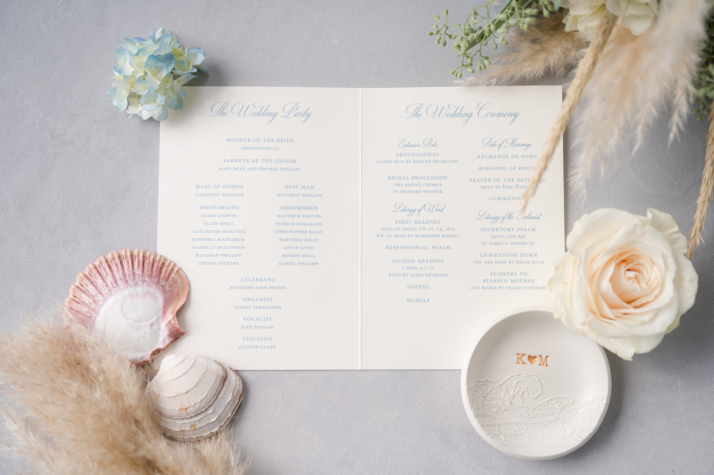 Softly styled wedding program surrounded by delicate florals, seashells, and airy textures, creating a romantic coastal inspired detail scene.