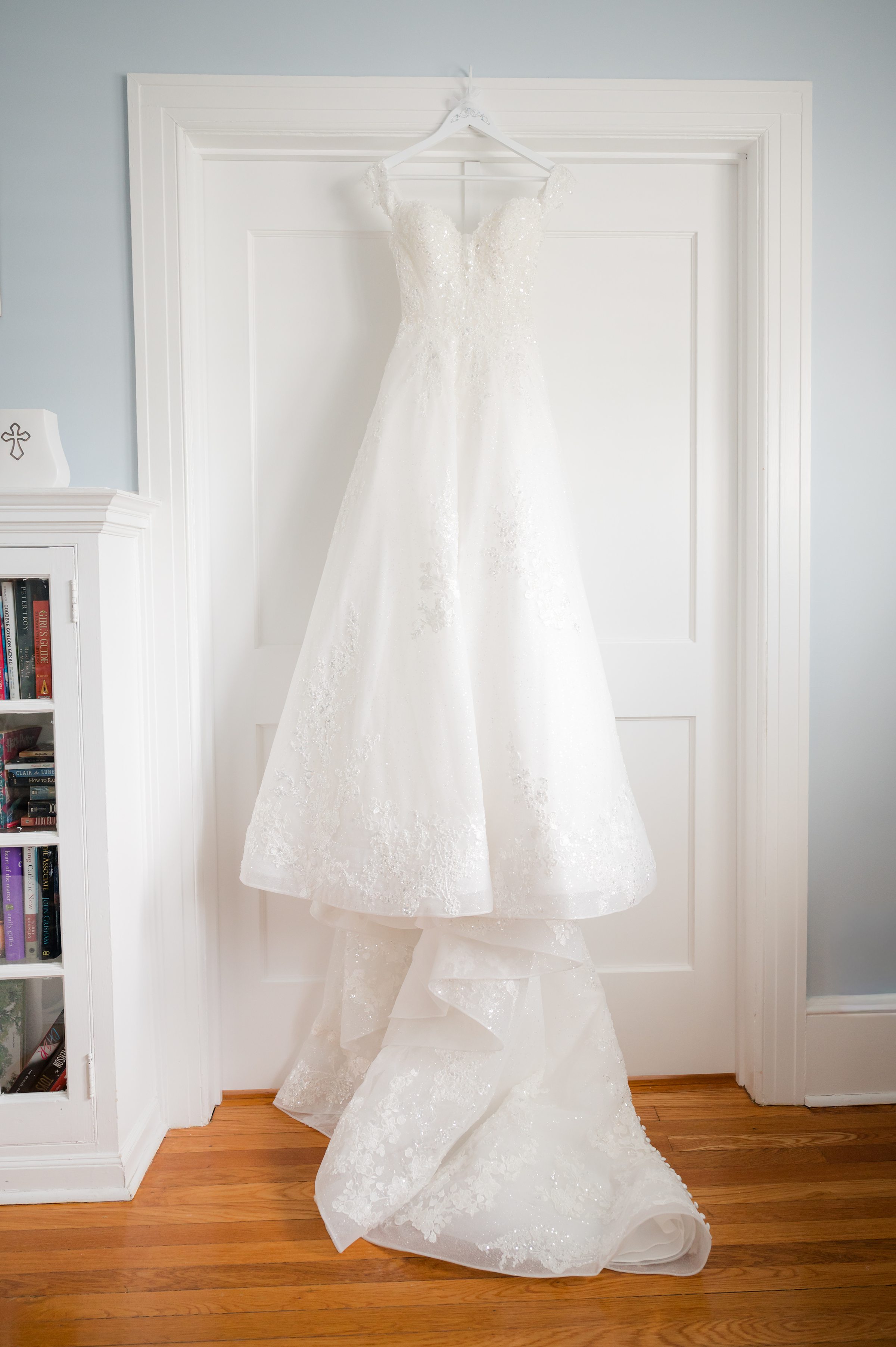 Romantic lace wedding gown hanging gracefully on a door, softly lit and waiting for the bride’s special moment.