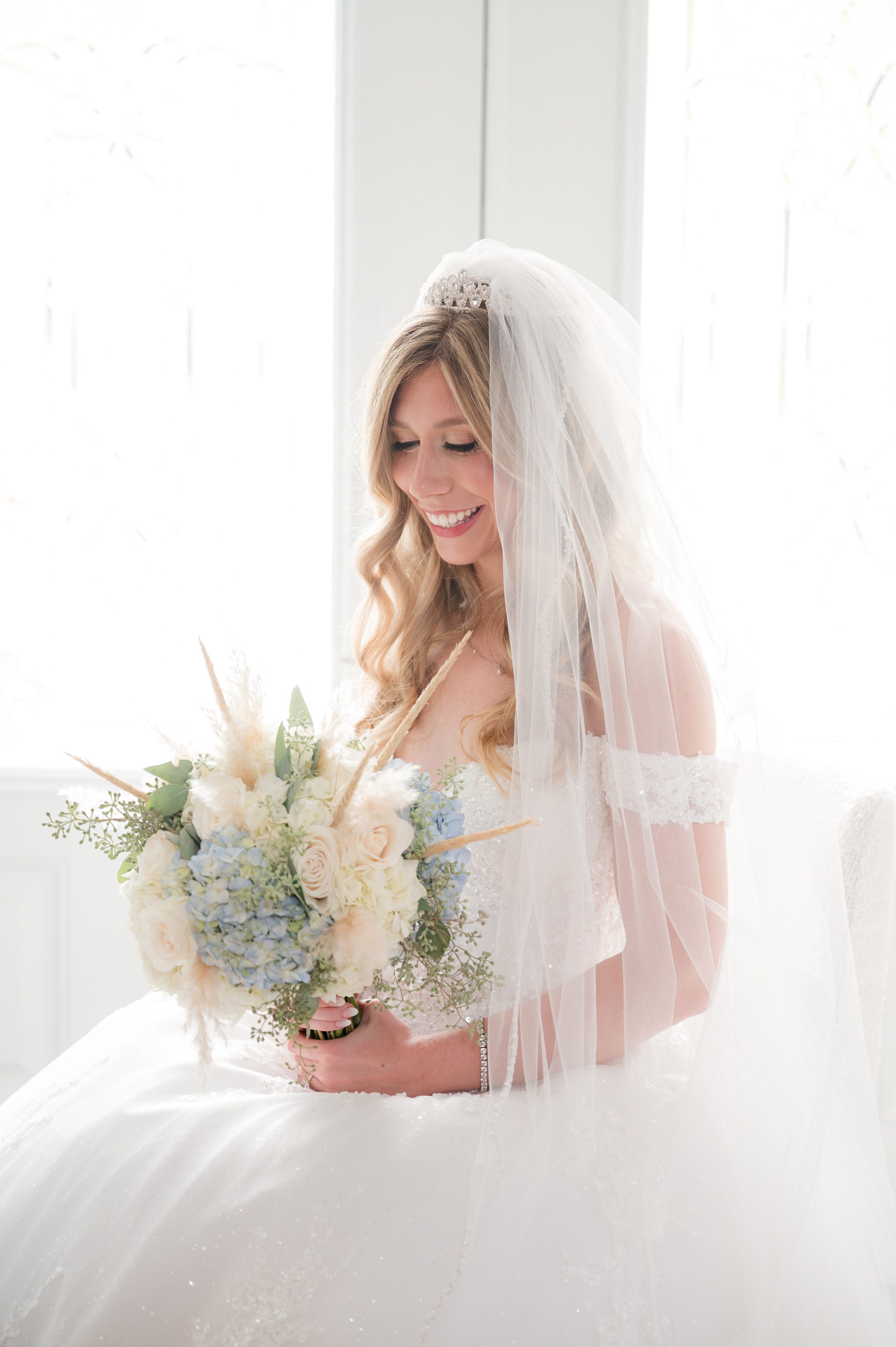 Bride in a veil holding a romantic bouquet of pastel blooms, capturing a tender and joyful moment before the ceremony.
