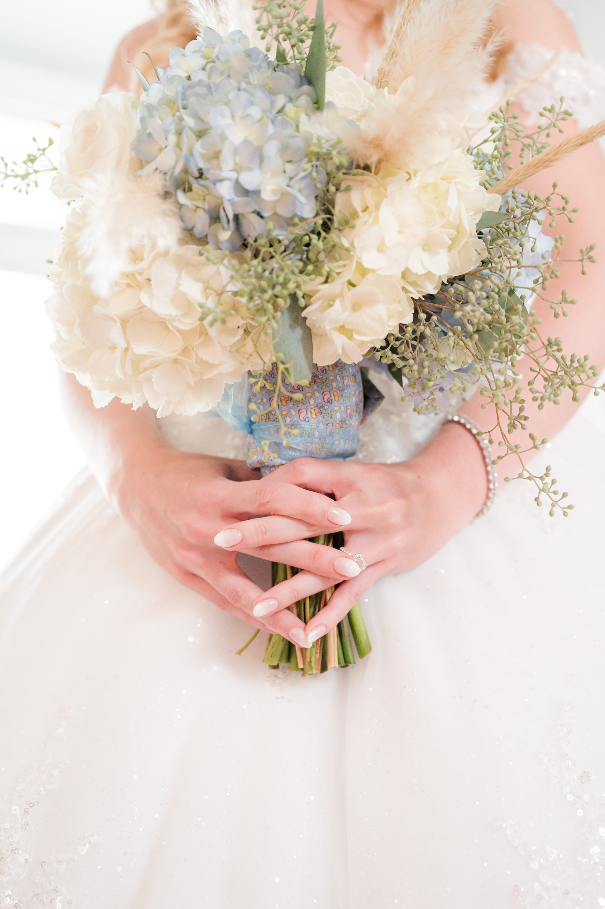 Bride’s hands gently holding a soft, romantic bouquet of hydrangeas and delicate blooms, her wedding ring subtly sparkling.