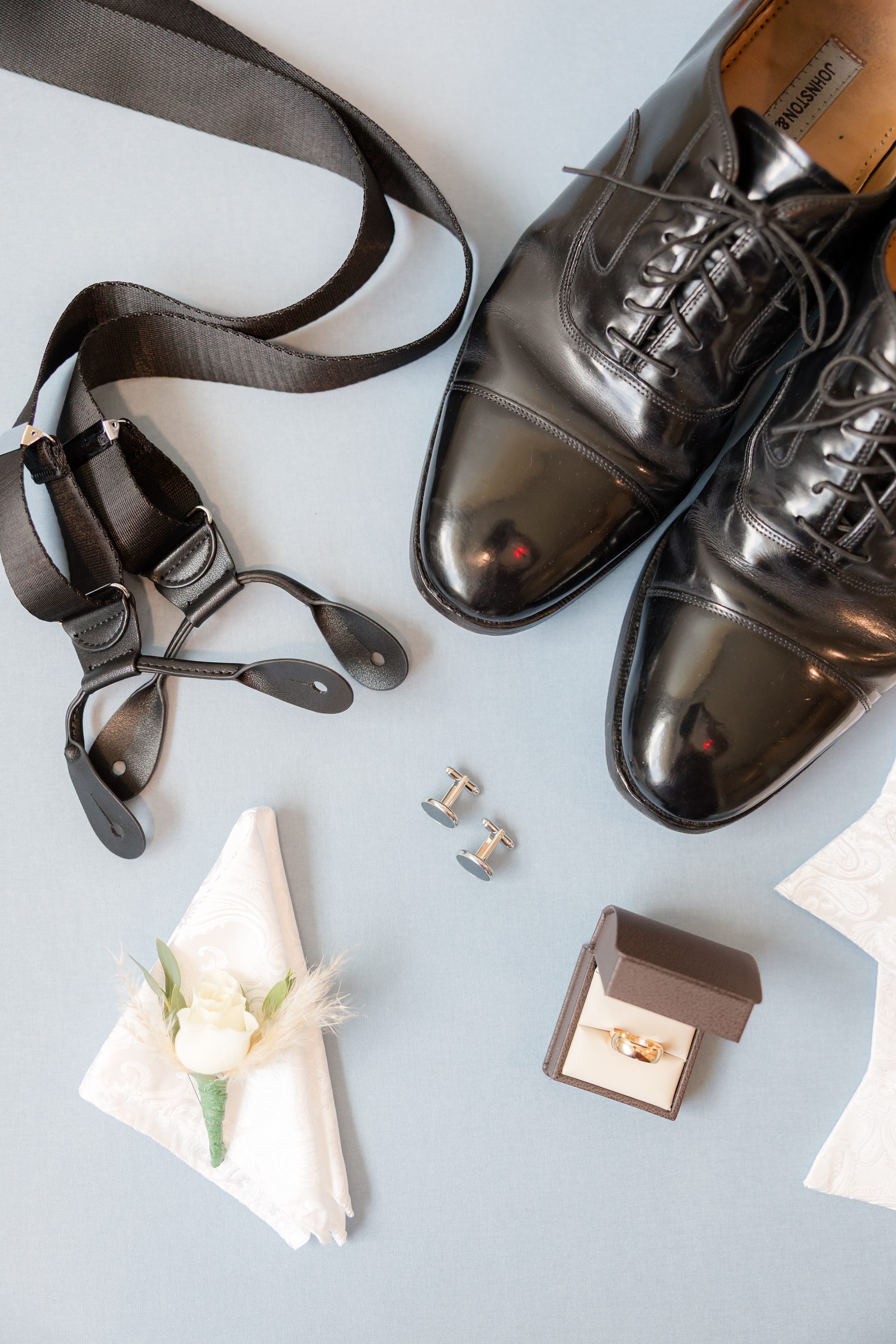 Groom’s polished black dress shoes, suspenders, cufflinks, and boutonniere, thoughtfully styled for a timeless wedding look.