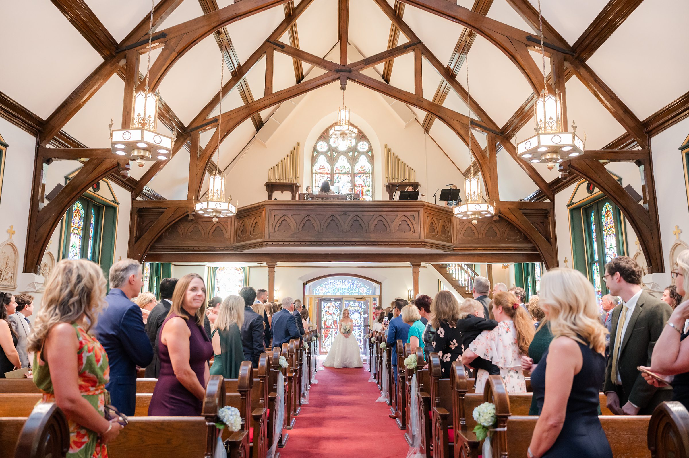 Bride walking down the aisle in a church filled with standing guests.