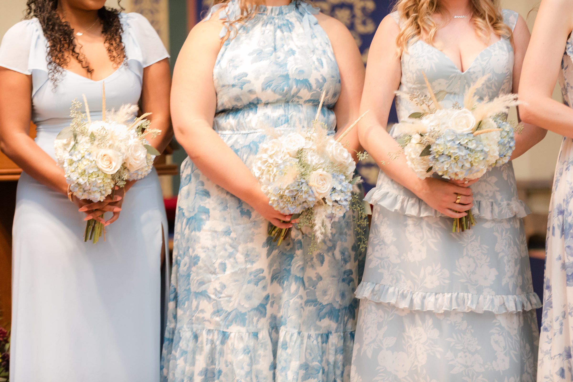 Bridesmaids holding soft blue and white floral bouquets against light blue dresses.