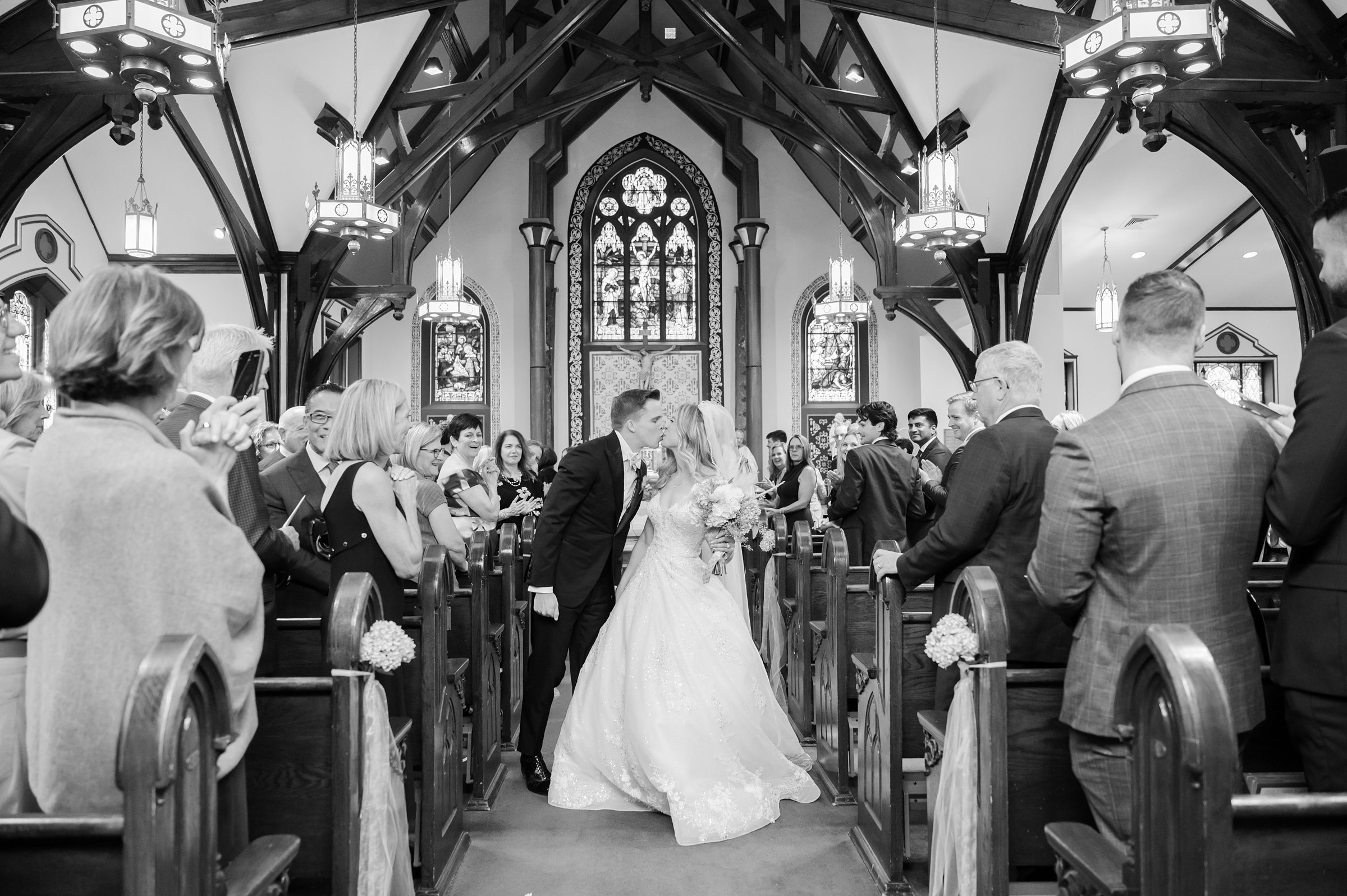 Bride and groom kiss in the aisle of a church while guests stand and watch from the pews.