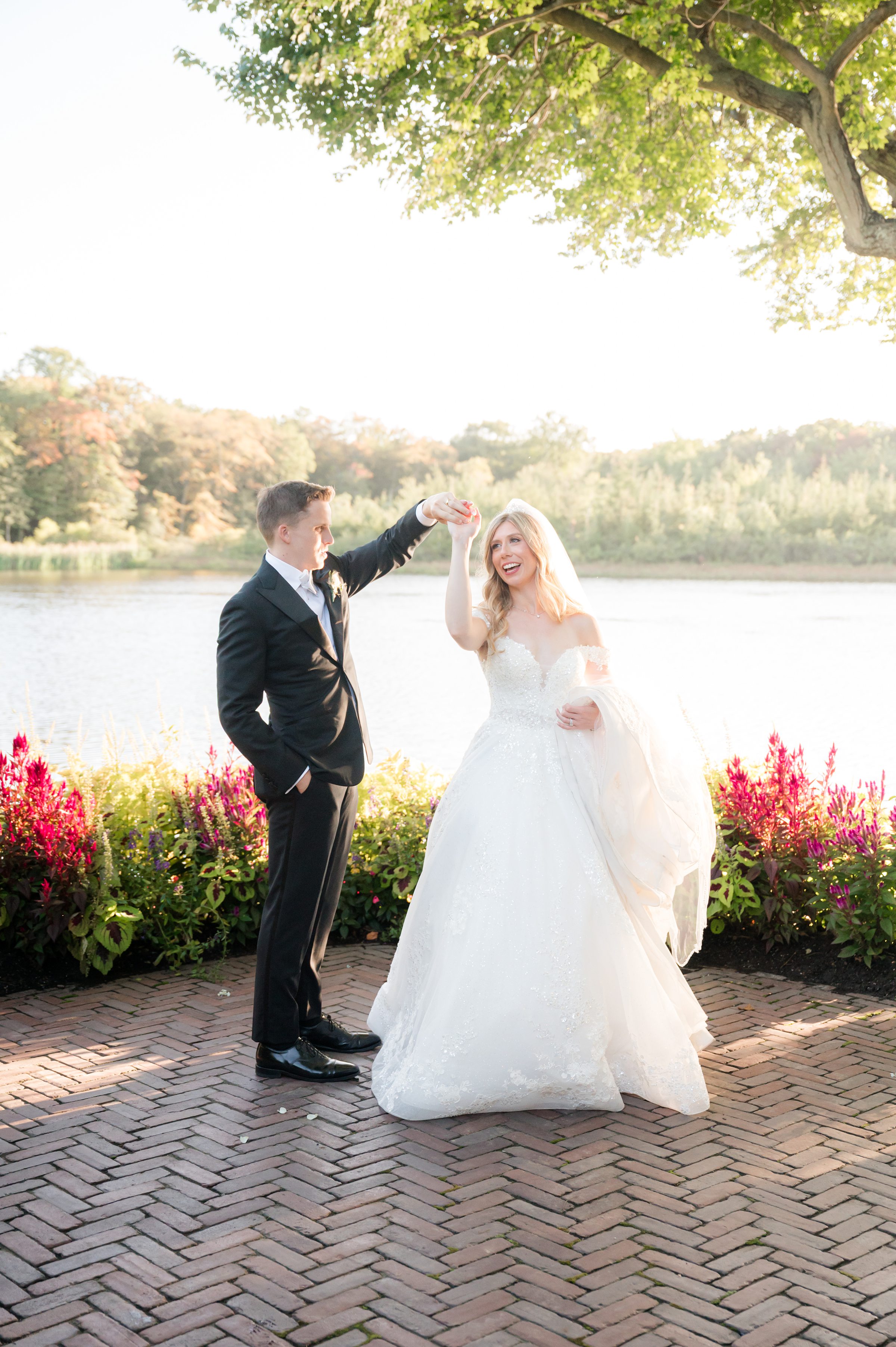 Bride twirling gracefully as the groom lifts her hand, capturing a playful, romantic moment by the water.