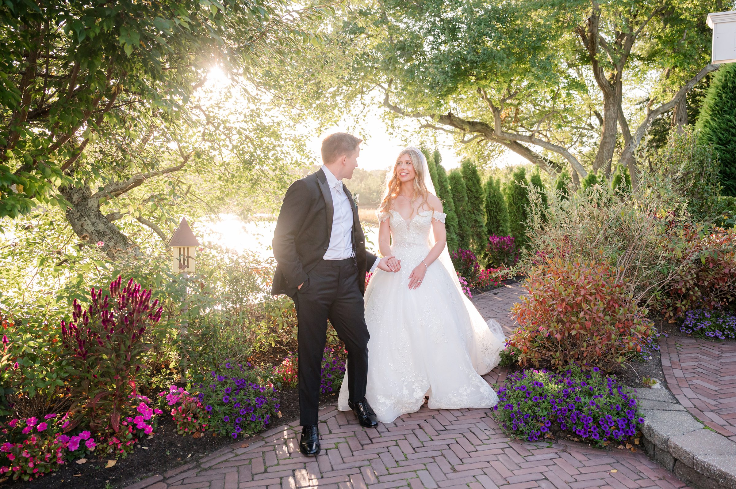 Bride and groom walking together through a sunlit garden, surrounded by vibrant blooms and soft greenery.