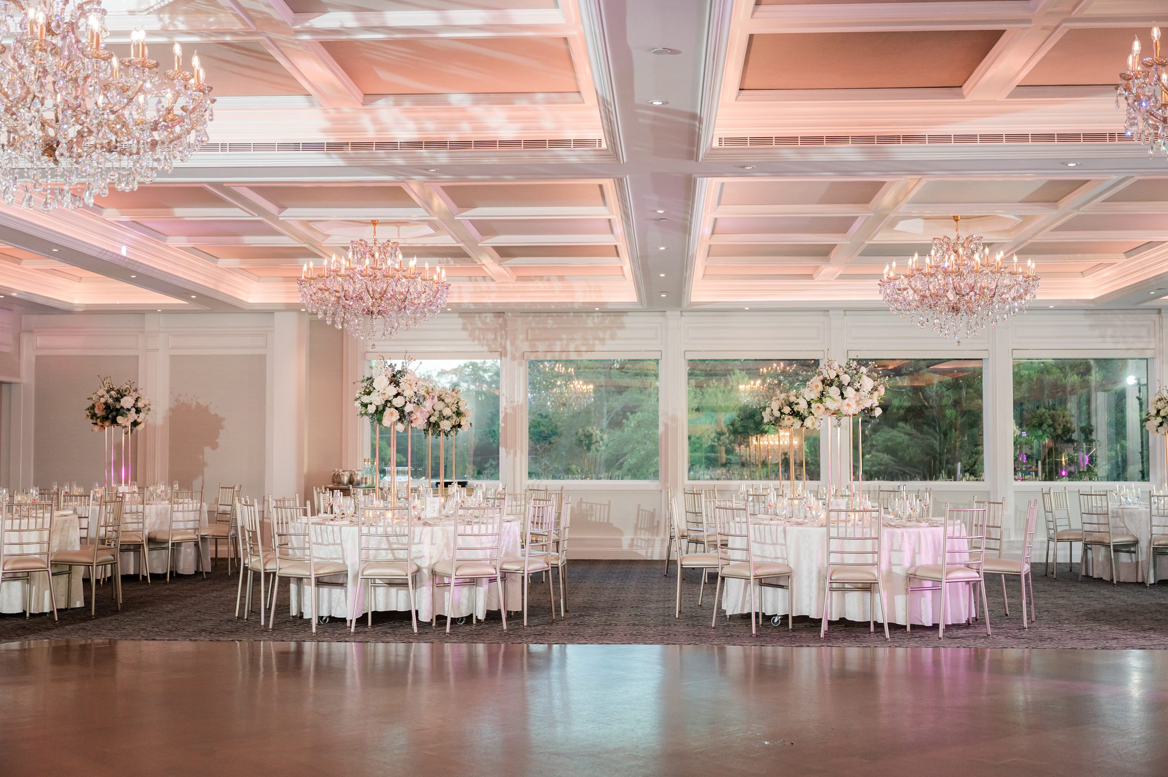 Grand wedding reception space filled with sparkling chandeliers, soft pink lighting, and beautifully set tables awaiting guests.