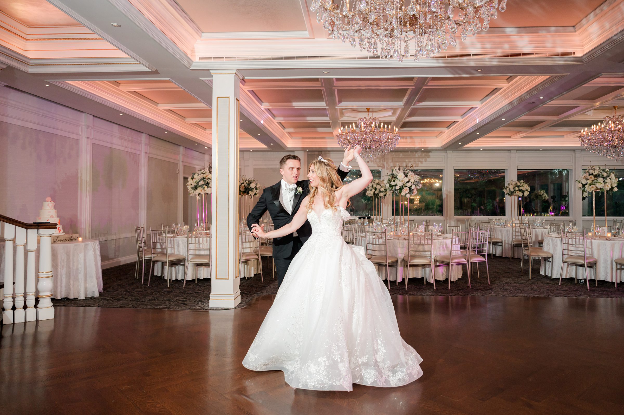 Bride twirls as the groom leads her across the dance floor in a spacious reception hall.