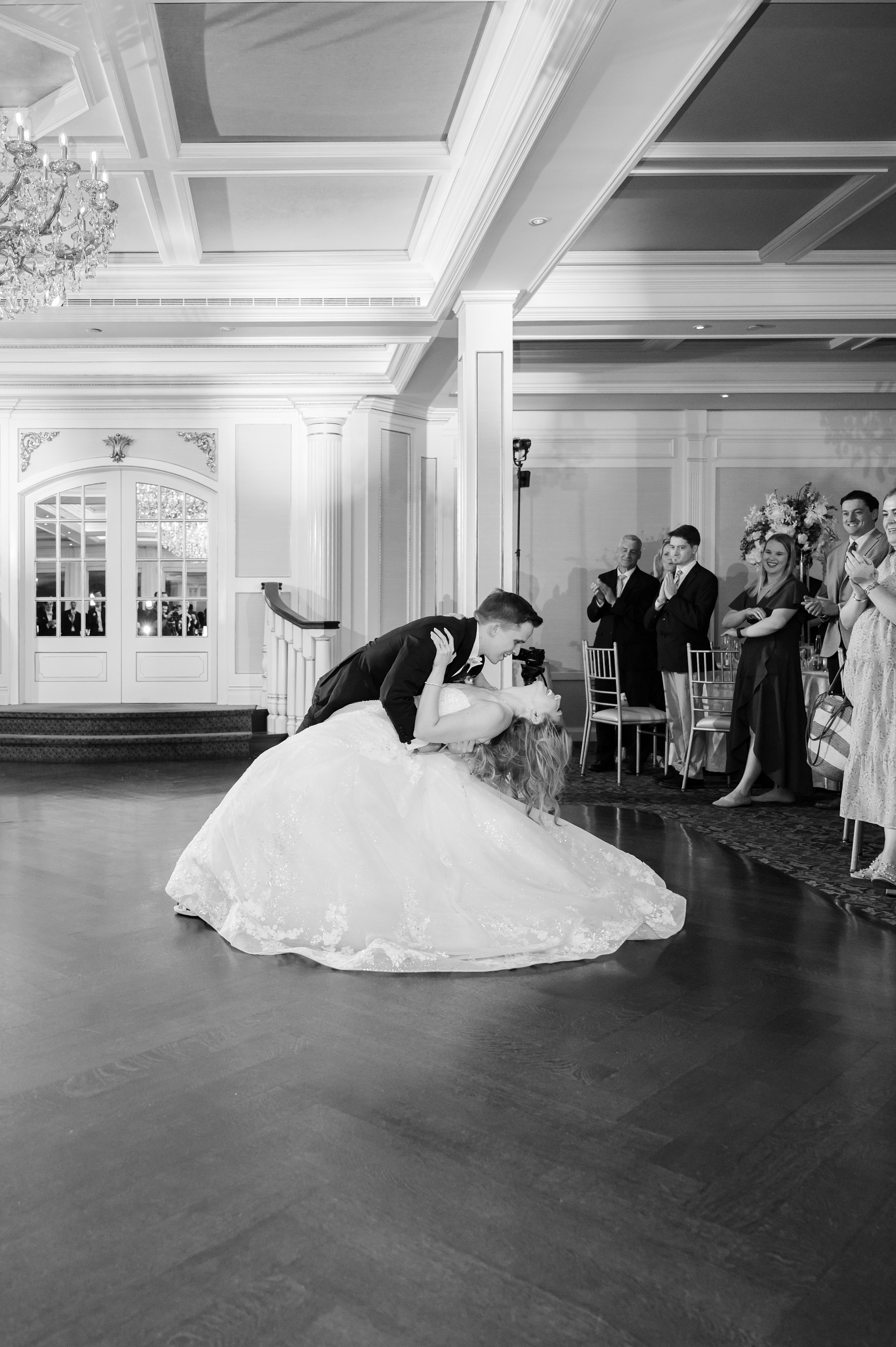 Groom dips the bride dramatically during their first dance while guests watch and applaud.