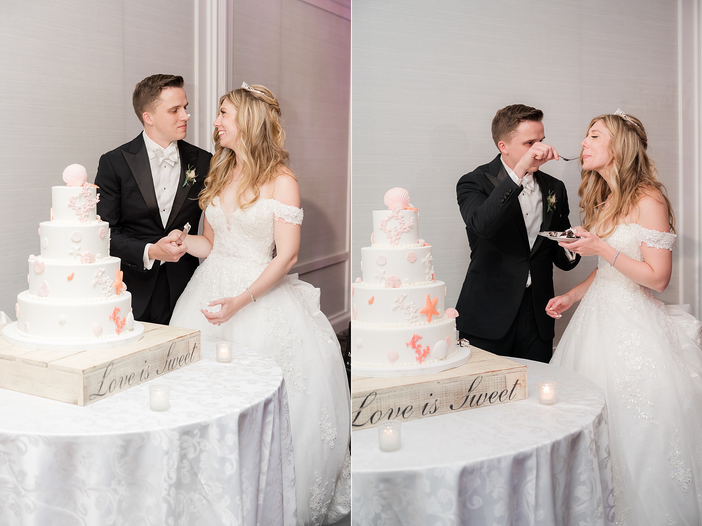 Bride and groom beside their tiered wedding cake and smiling together while holding the cake knife, then playfully feeding each other a bite.
