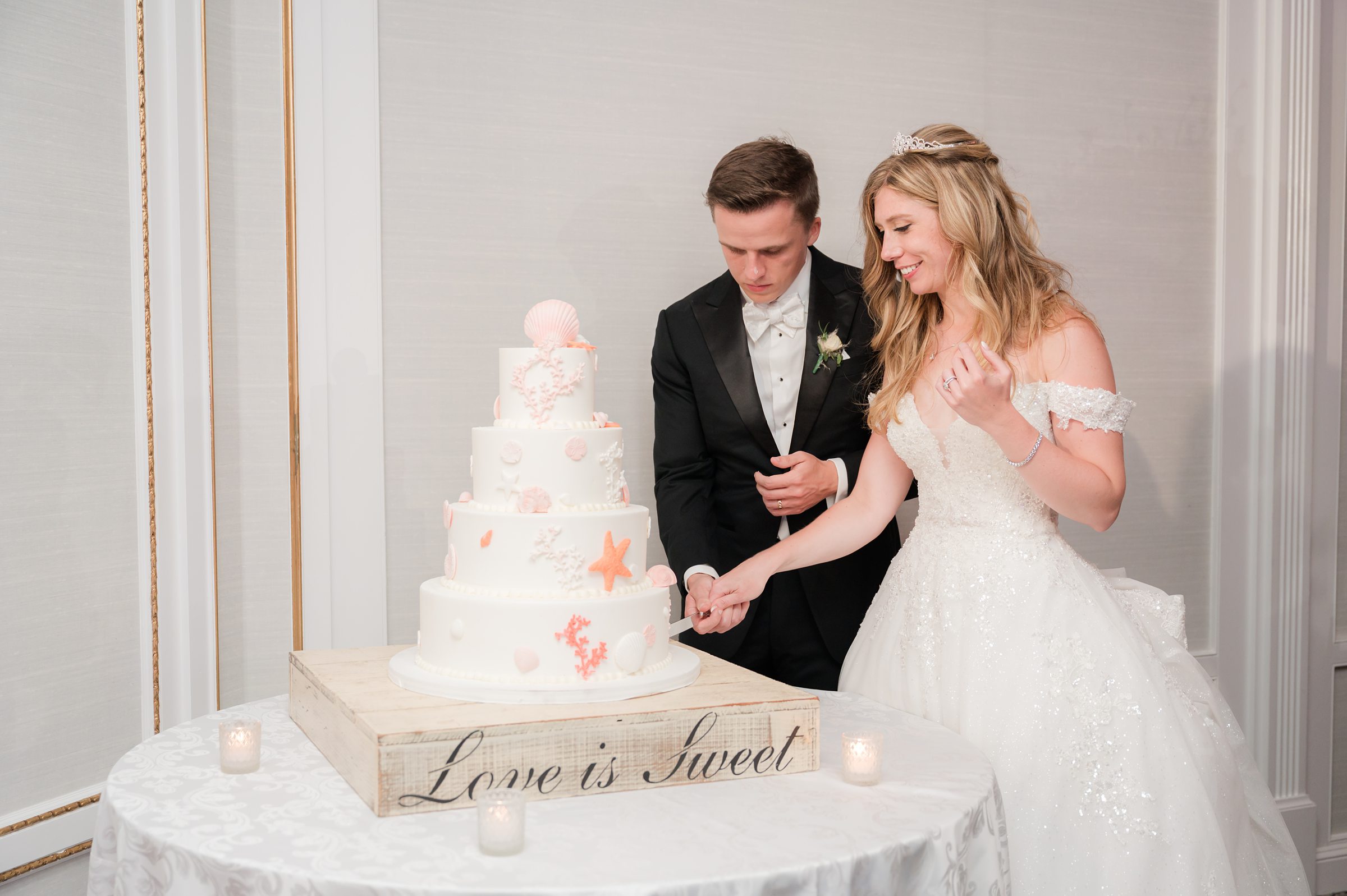 Bride and groom cut their wedding cake together, smiling.