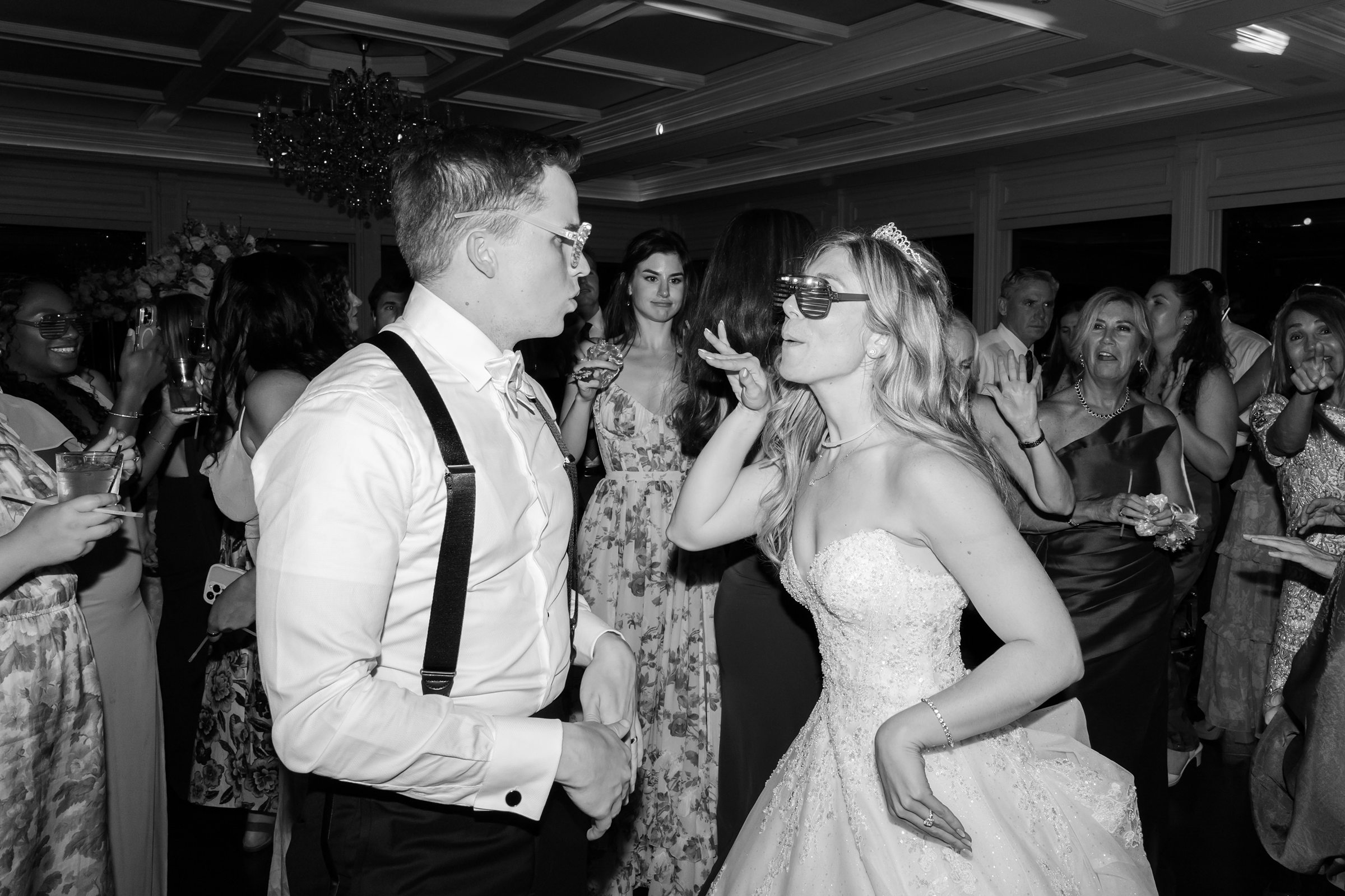 Bride and groom dance closely on a crowded dance floor, surrounded by guests.