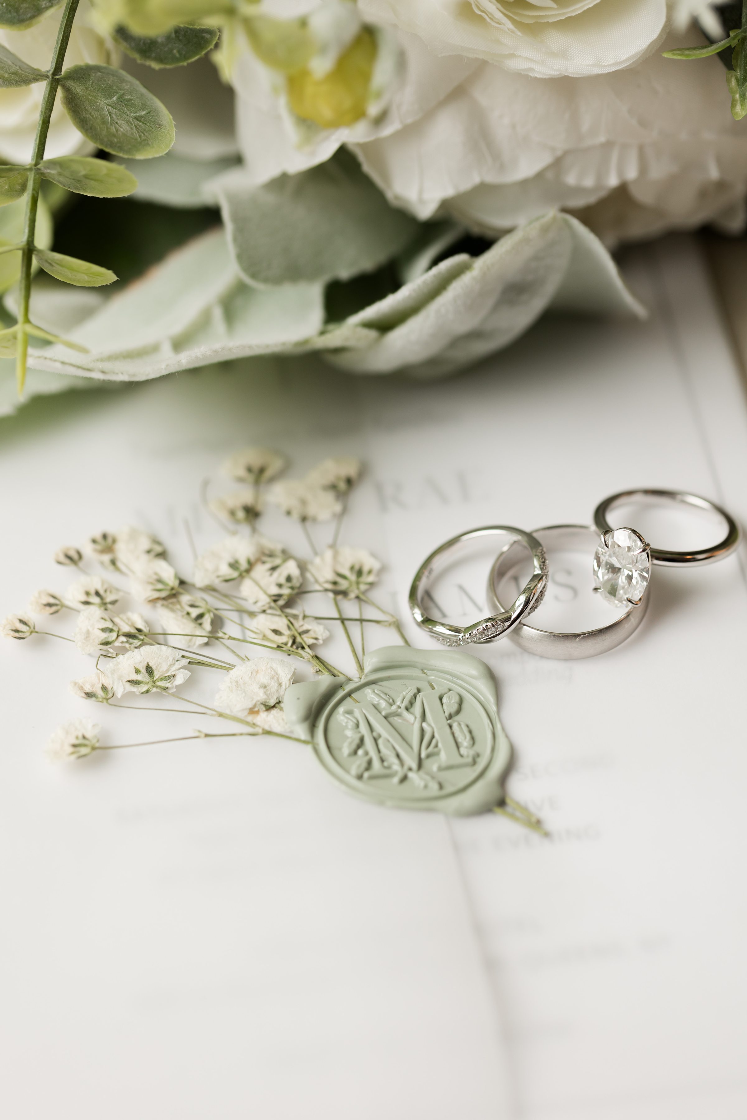 Wedding rings on paper with greenery and wax seal detail.