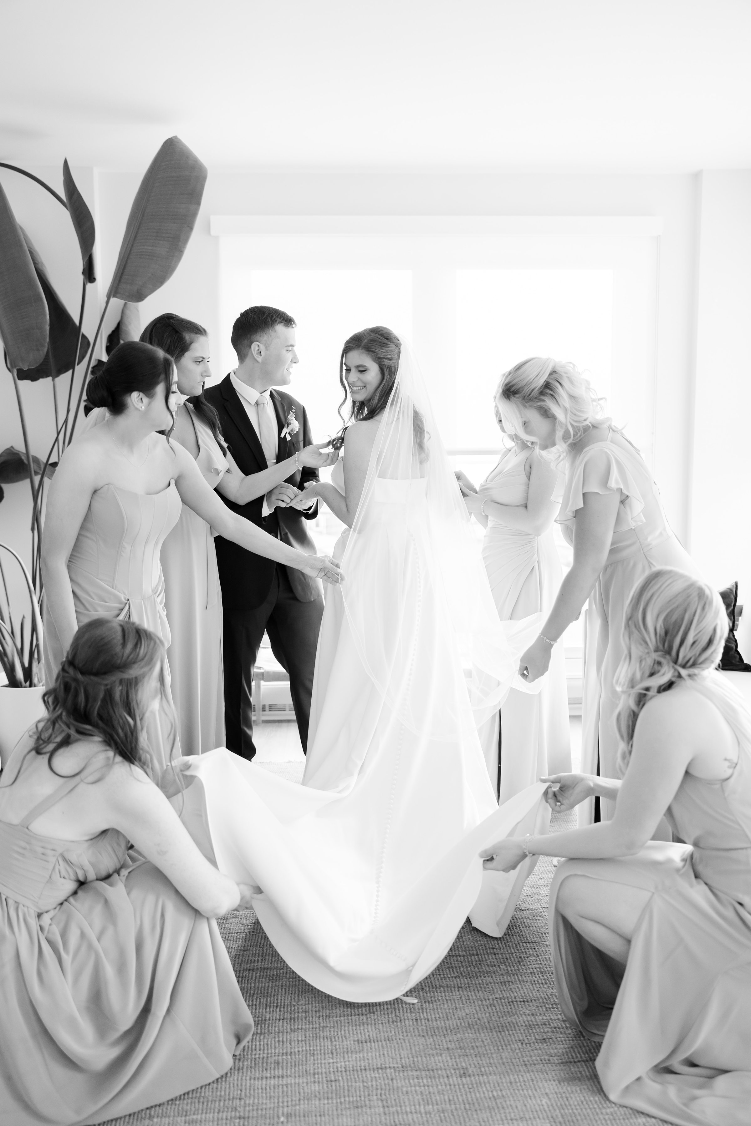 Bridesmaids gathered around the bride, helping adjust her wedding dress and veil.