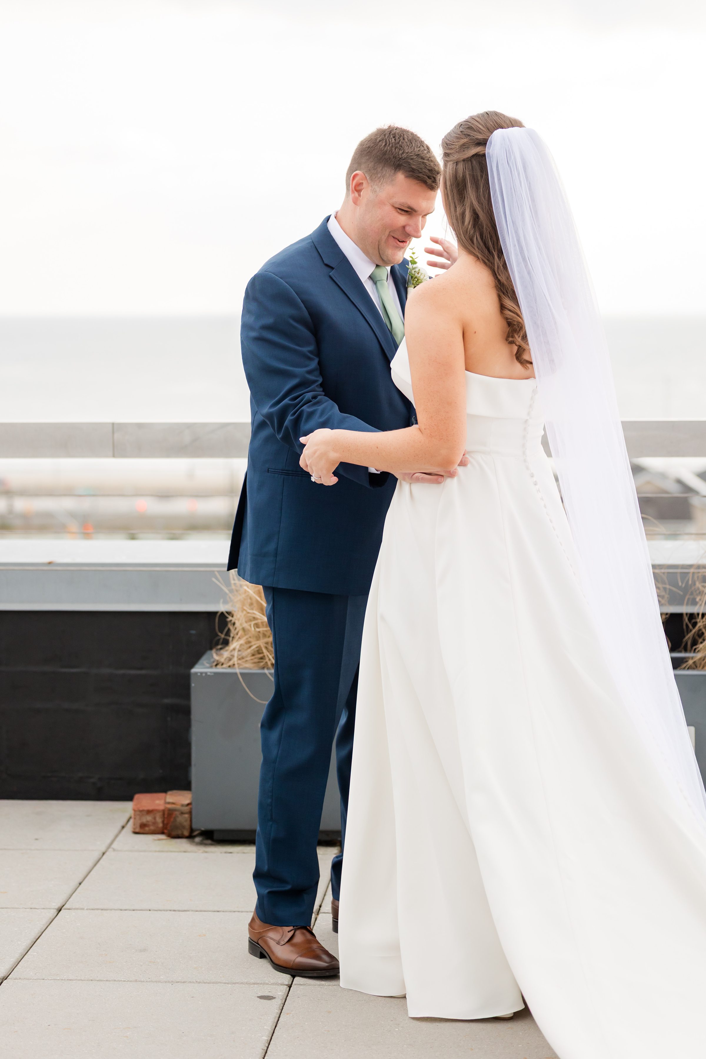 Groom holding bride’s hands as they stand facing each other on rooftop.
