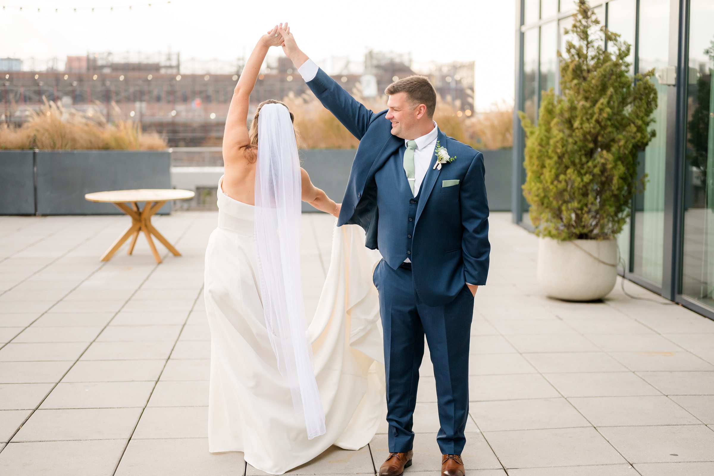 Groom twirling the bride as she lifts her arm, veil flowing, on a rooftop terrace.