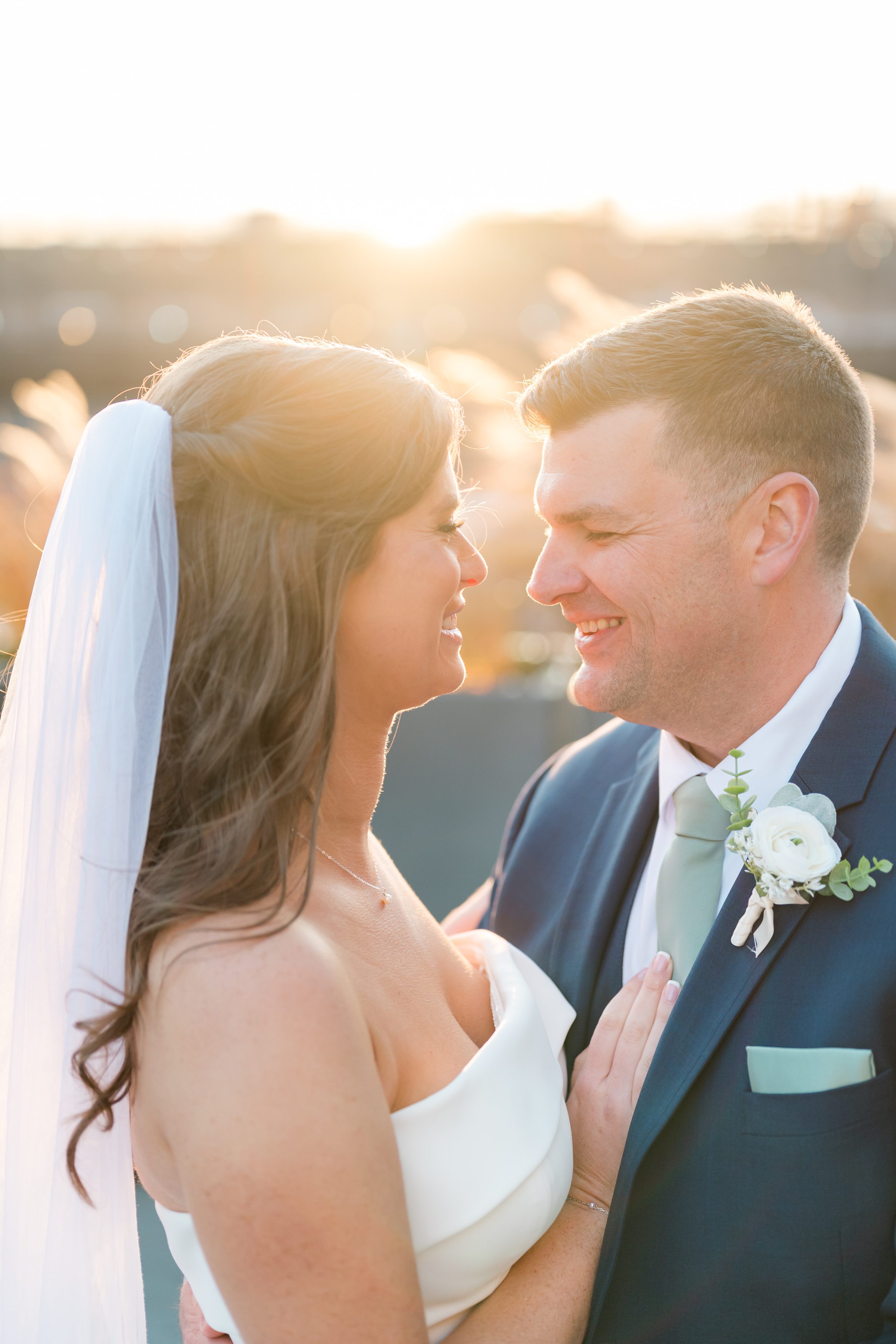 Bride and groom smiling at each other in warm sunset light.