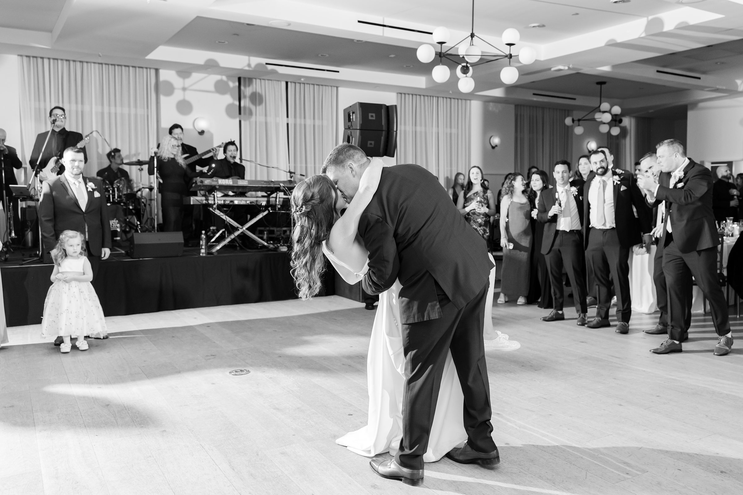 Groom dips bride dramatically on the dance floor while guests watch and a live band plays in the background.