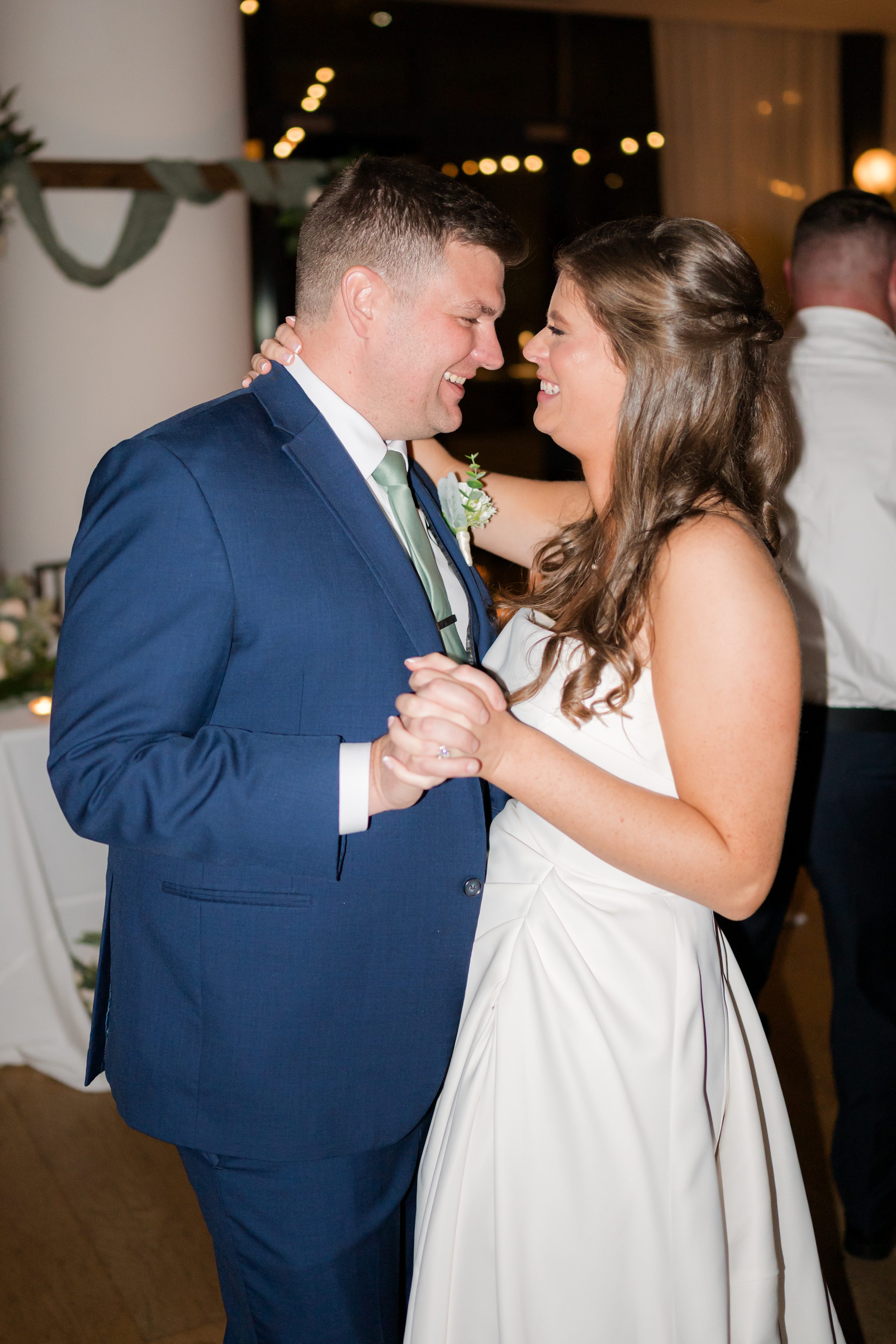 Bride and groom smile warmly at each other while sharing a close, intimate dance at their wedding reception.