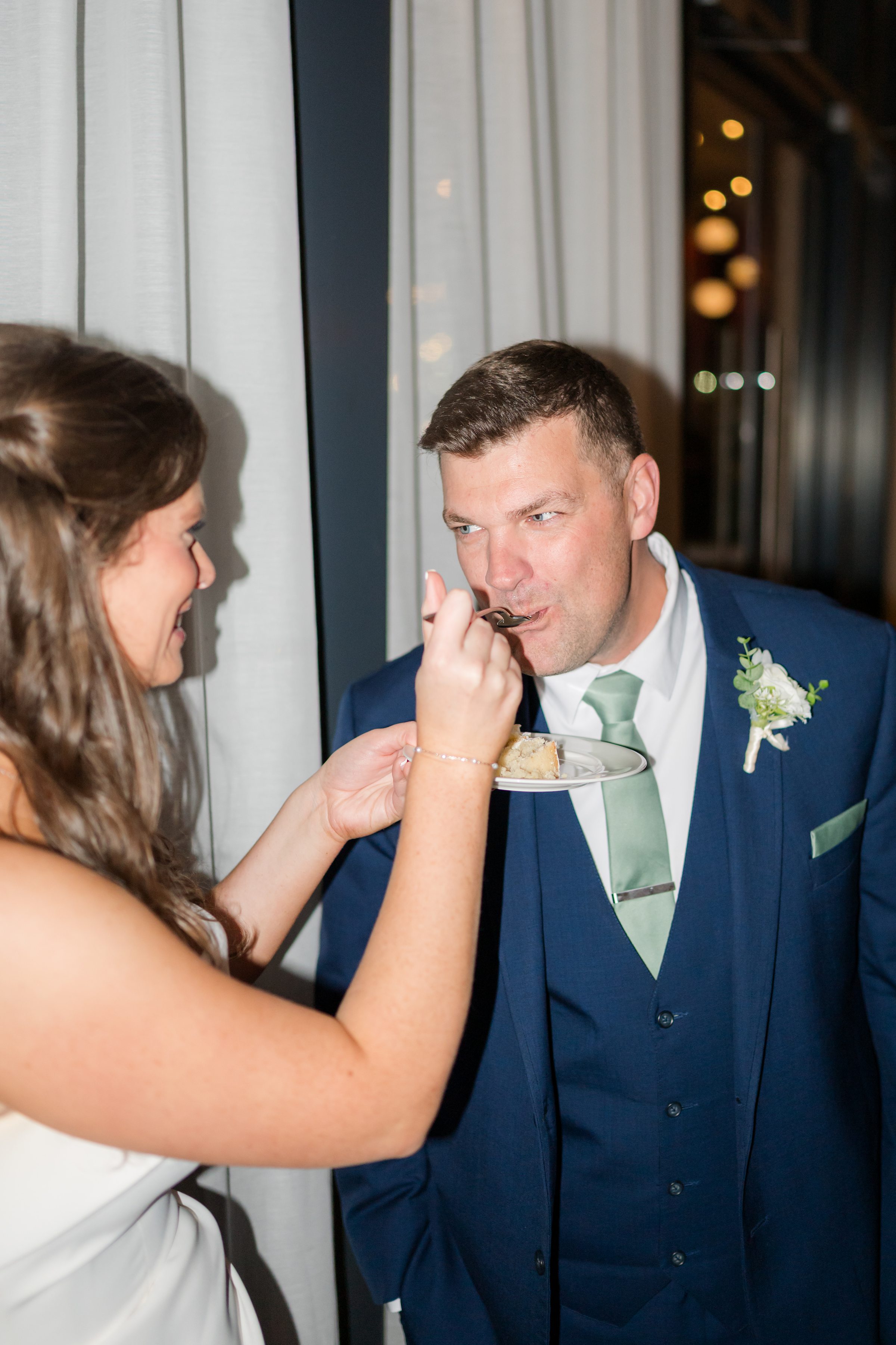 Bride feeds groom a bite of cake as they share a playful and affectionate moment during their wedding celebration.