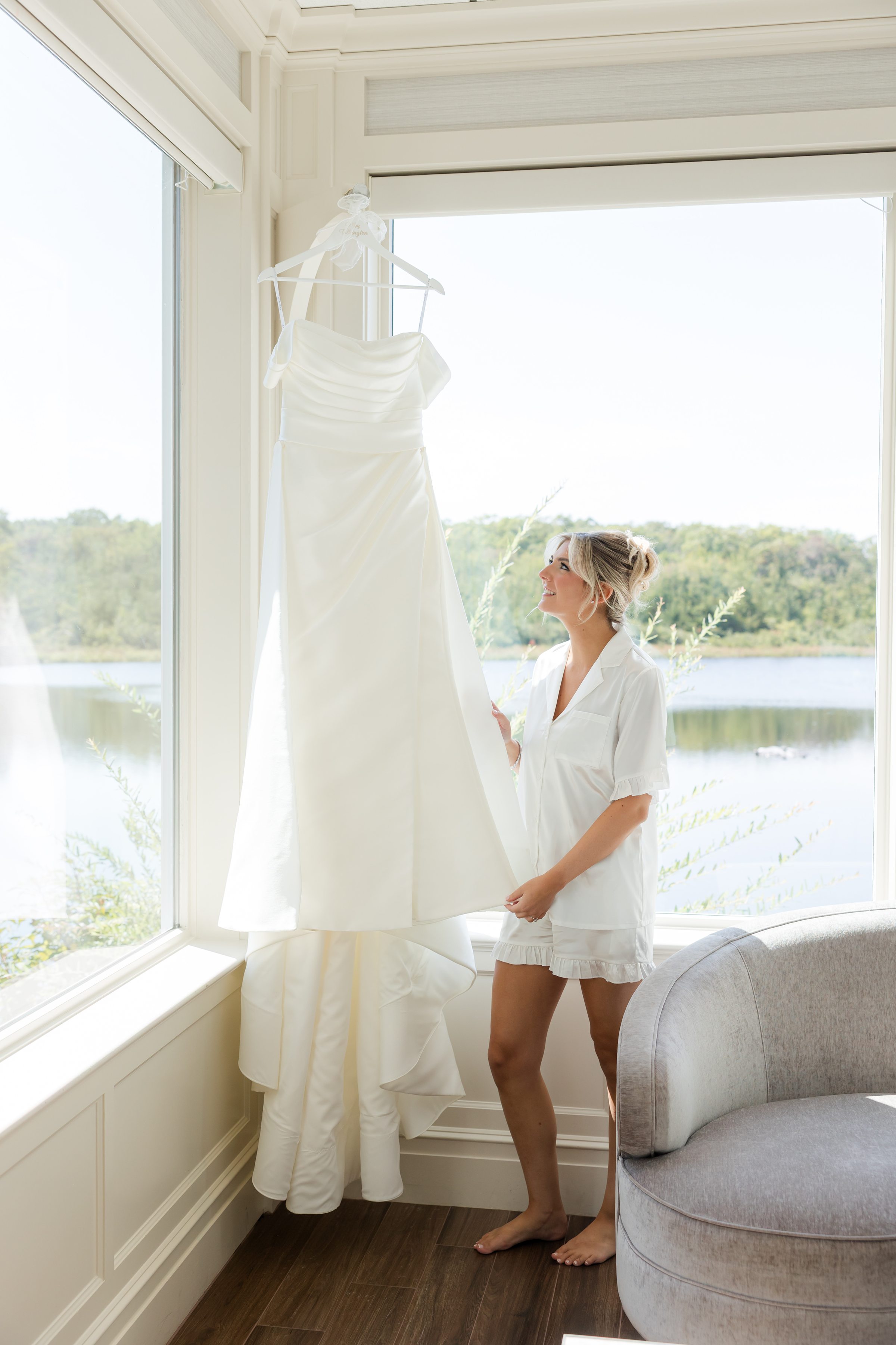 Bride admiring her wedding dress hanging in a sunlit window, a quiet and emotional moment before getting ready.