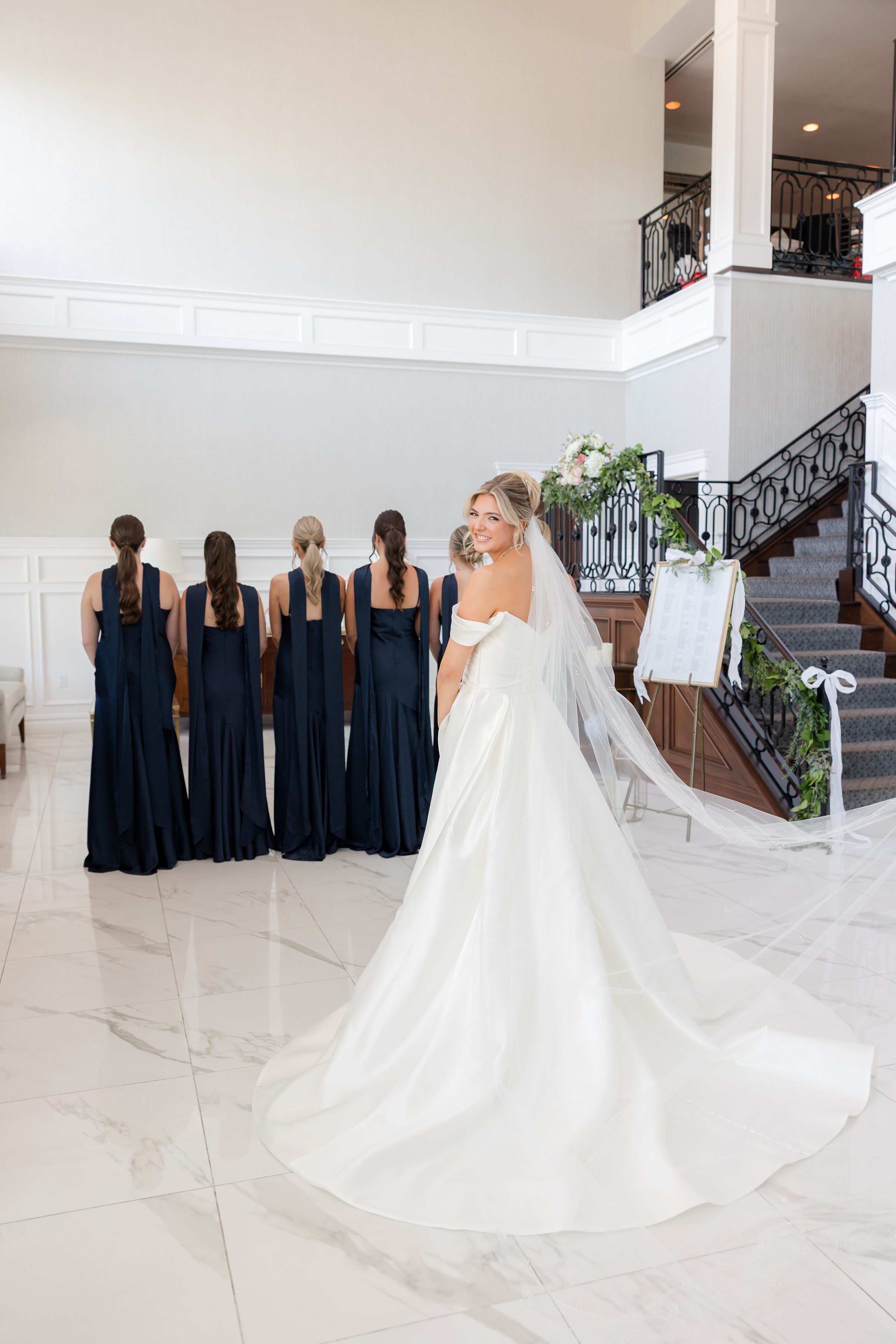 Bride turns back with a glowing smile while bridesmaids stand behind her, creating a soft, joyful pre-ceremony moment.