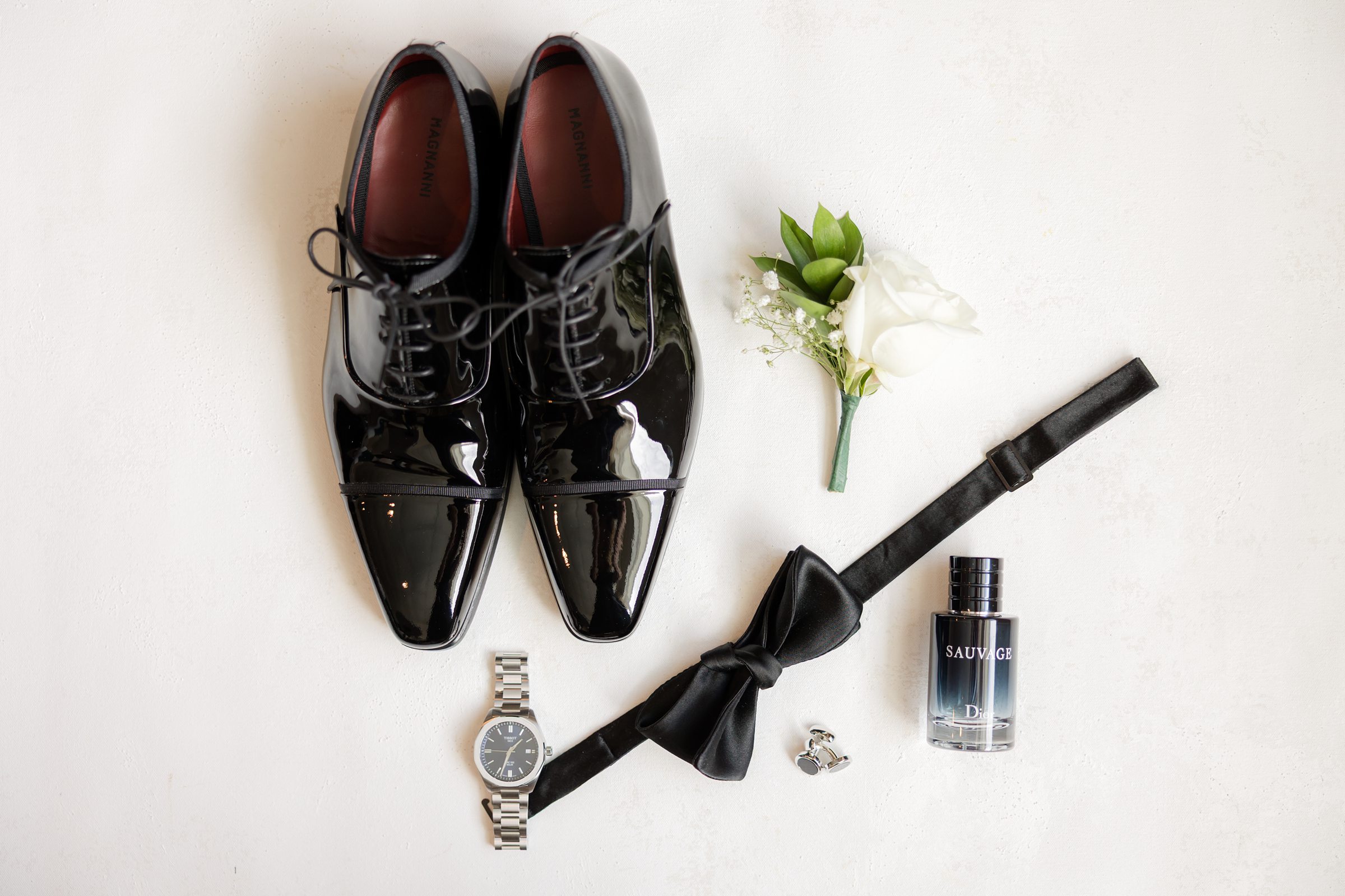 Groom’s wedding details featuring shoes, boutonniere, watch, and bow tie.