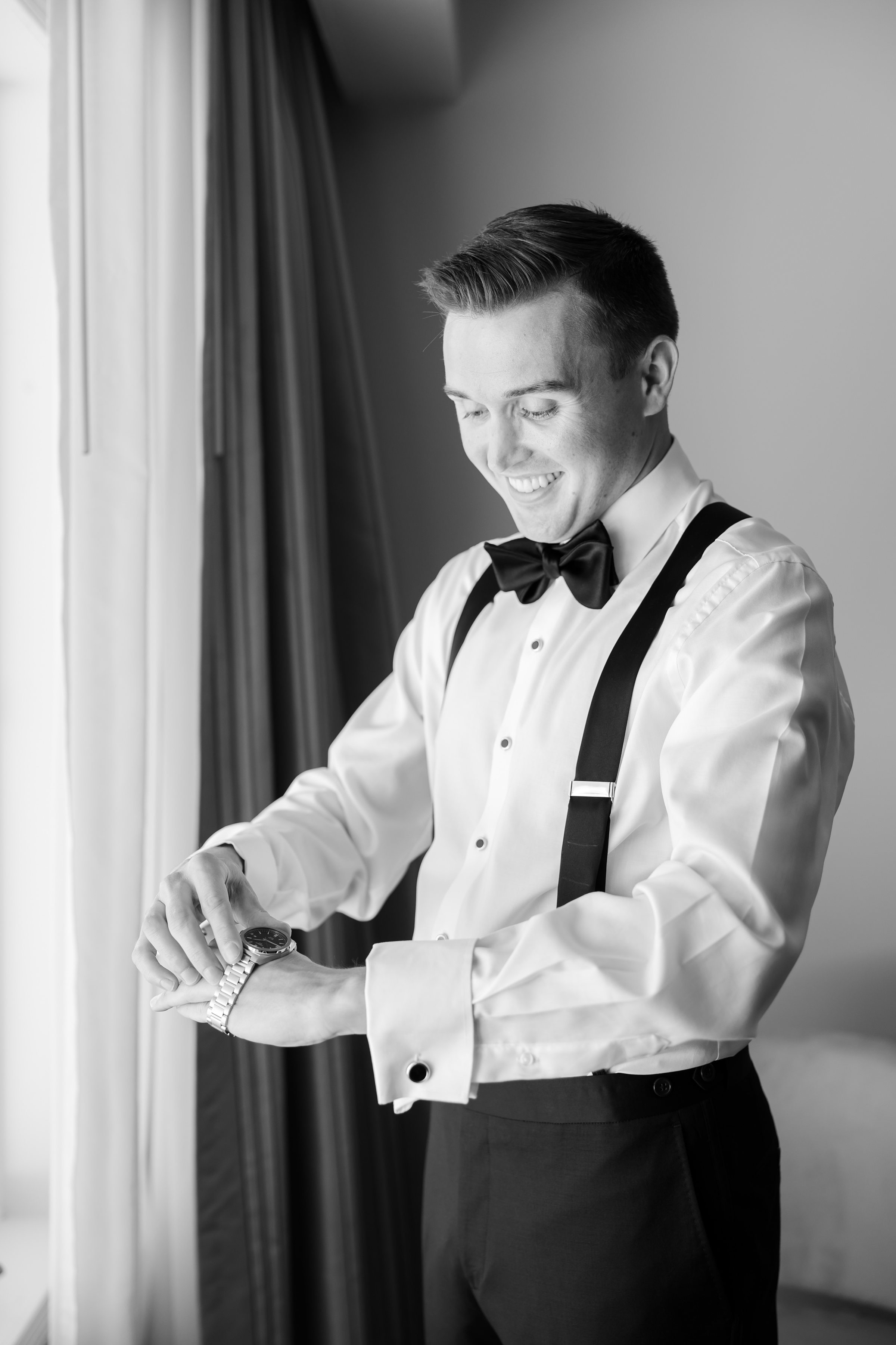 Groom smiles while fastening his watch in a timeless black-and-white portrait.
