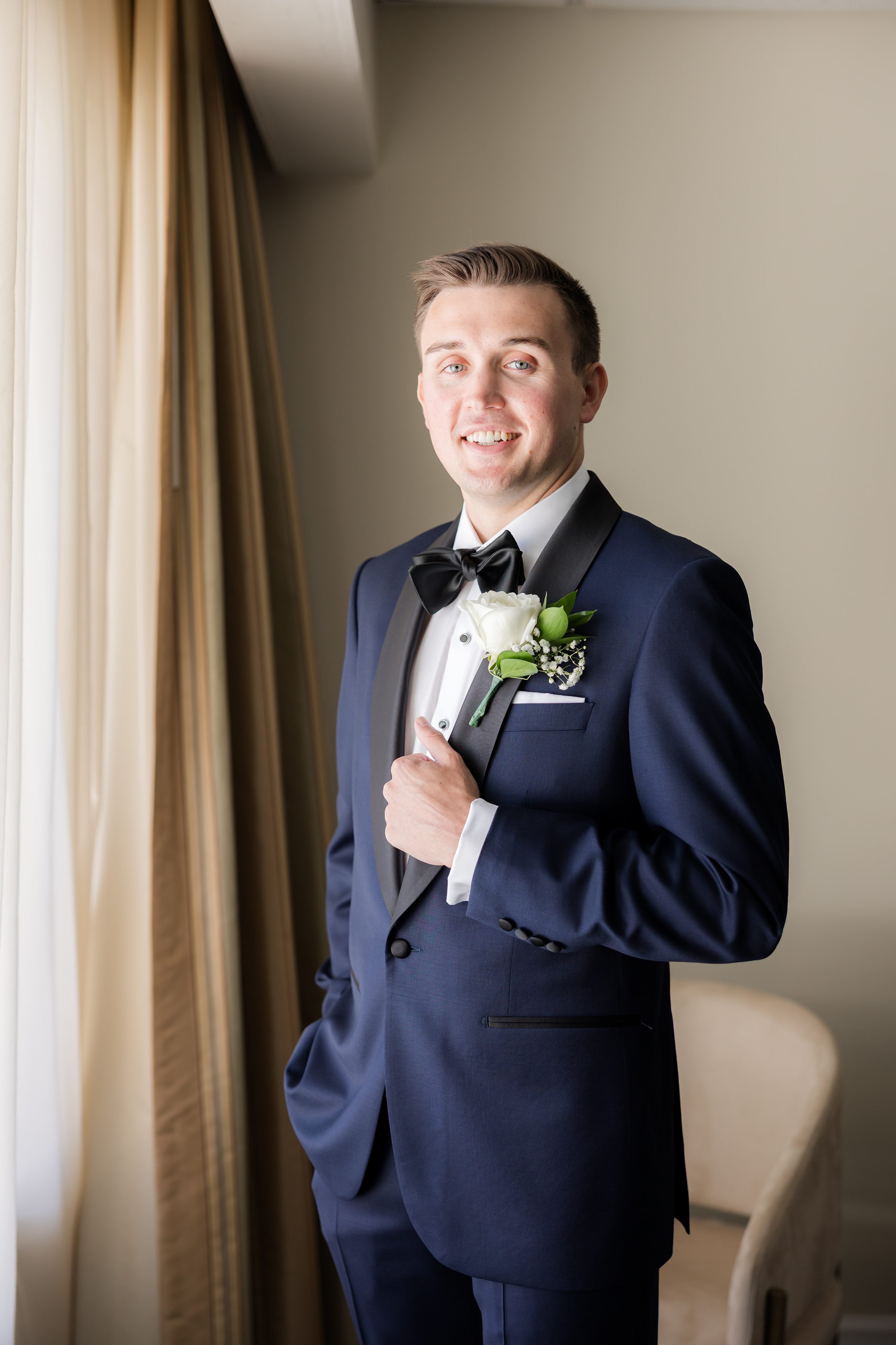 Groom stands by a window, softly lit, preparing for the wedding.