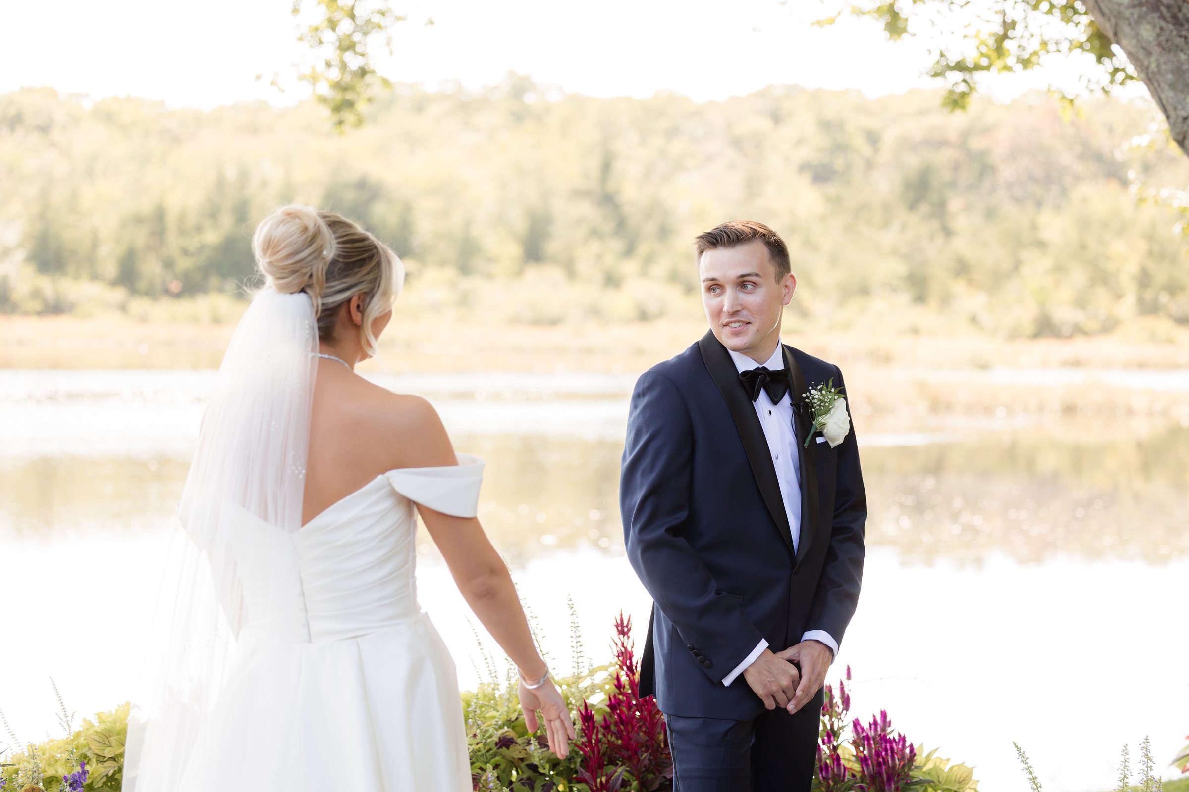 Groom smiles over his shoulder at the bride during a candid lakeside moment.
