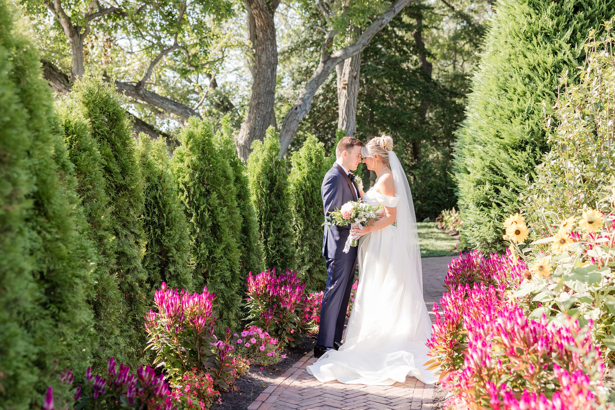Bride and groom share an intimate moment along a flower-lined path.