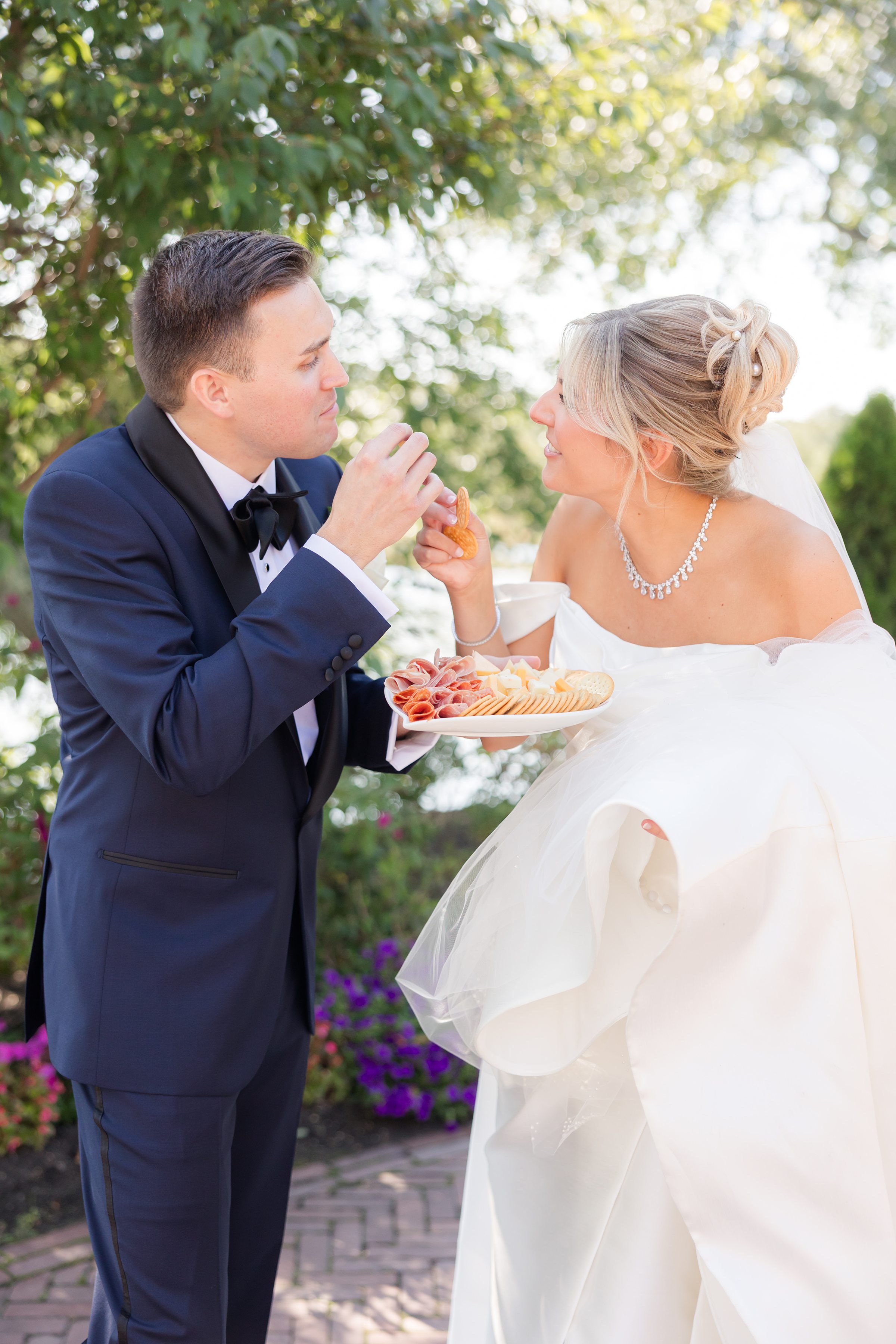 Bride and groom shares a playful moment, feeding each other appetizers in a garden setting.