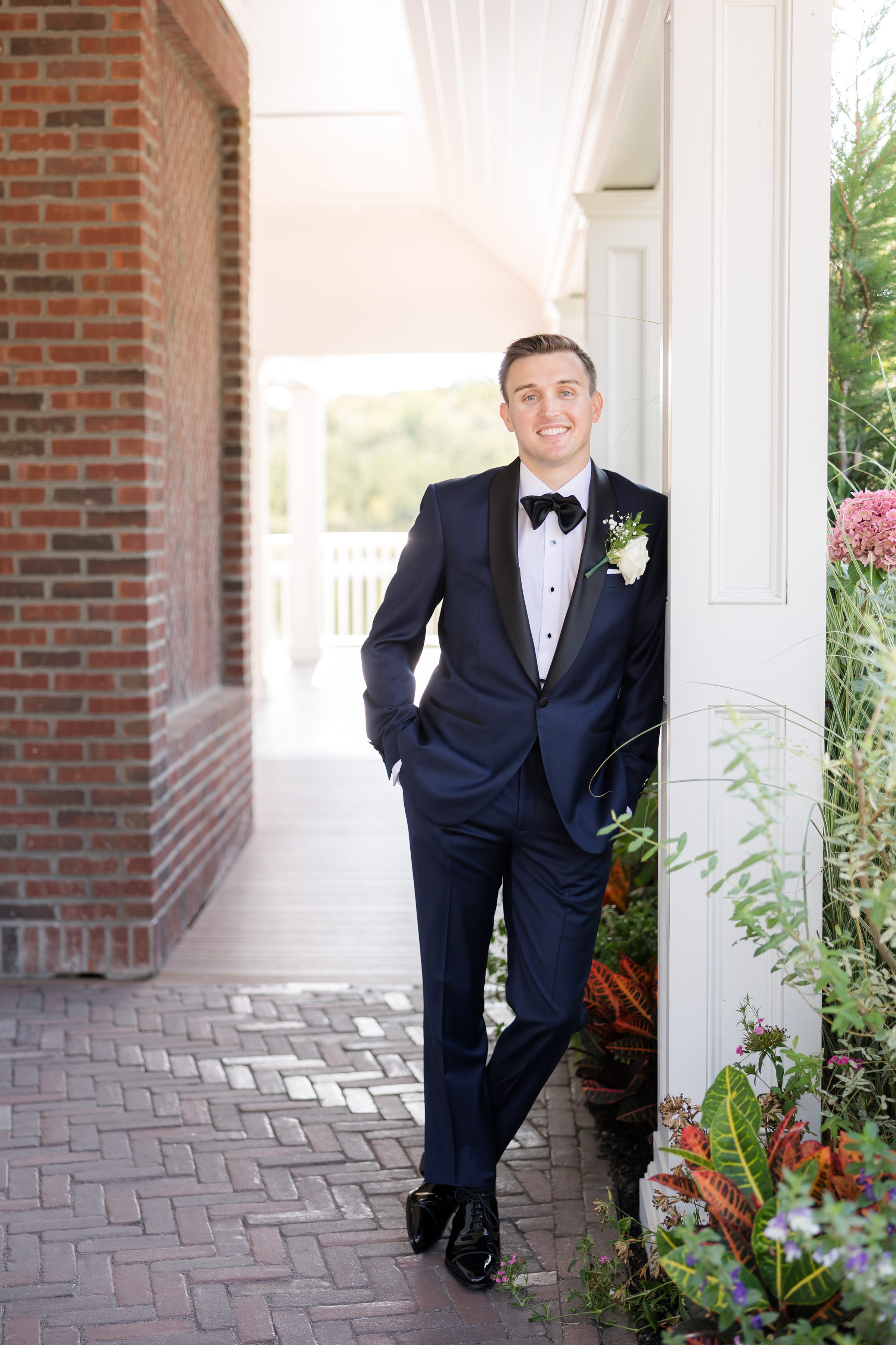 Groom leans casually against a column, looking relaxed and happy before the ceremony.