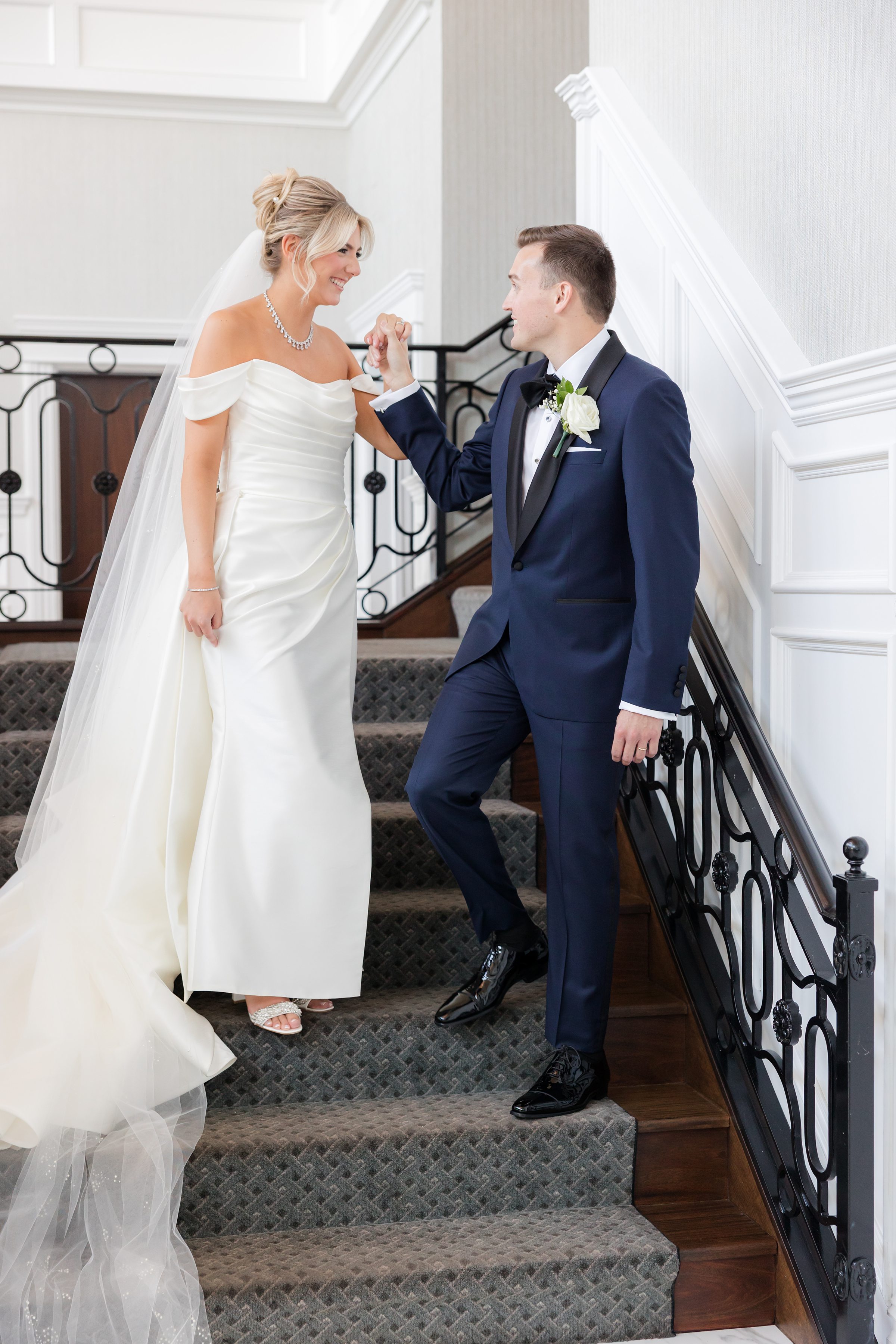 Bride and groom shares a quiet, romantic moment on an elegant indoor staircase, gazing at each other.