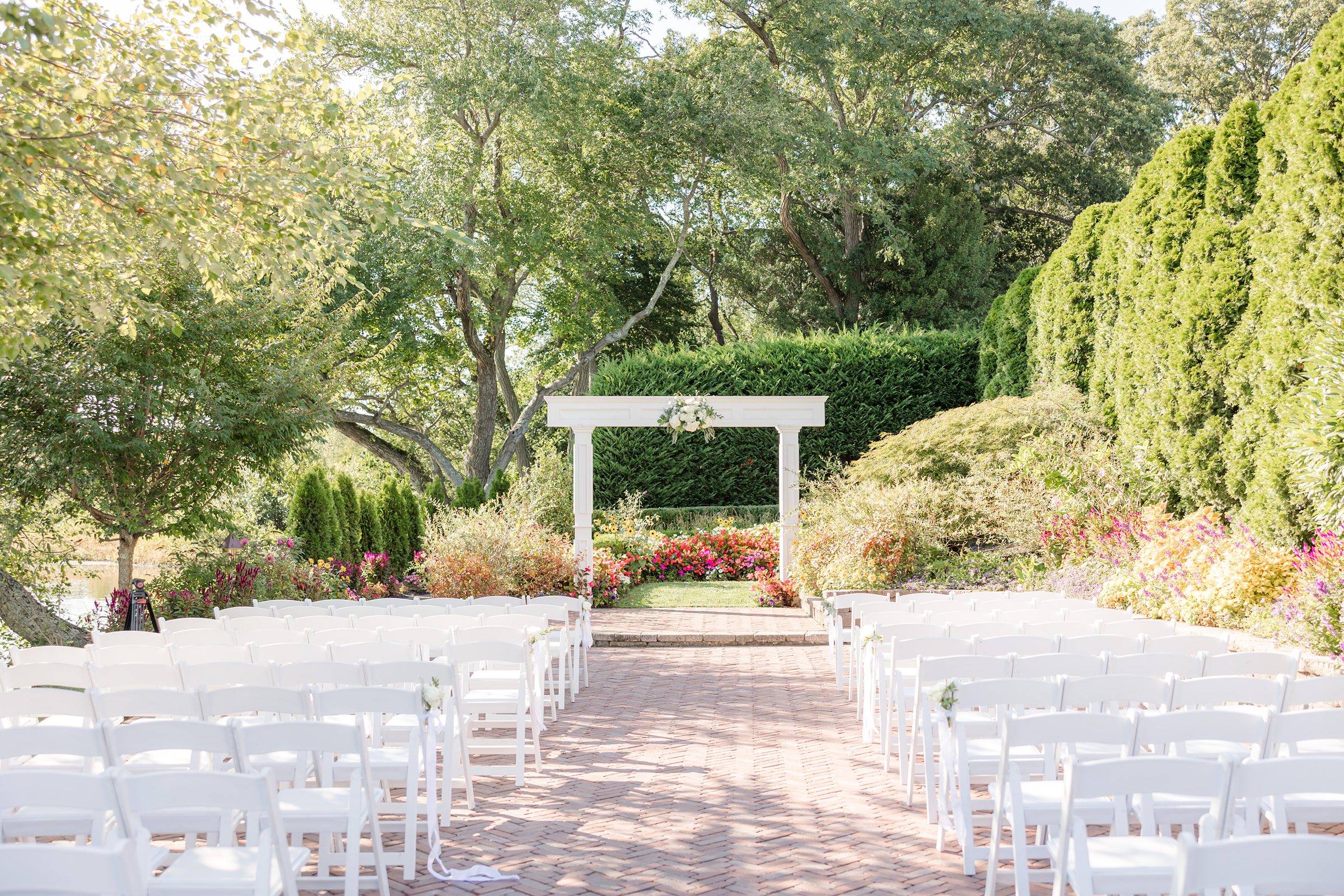 Wide view of an outdoor wedding ceremony with guests seated as the couple exchanges vows beneath a white arbor.