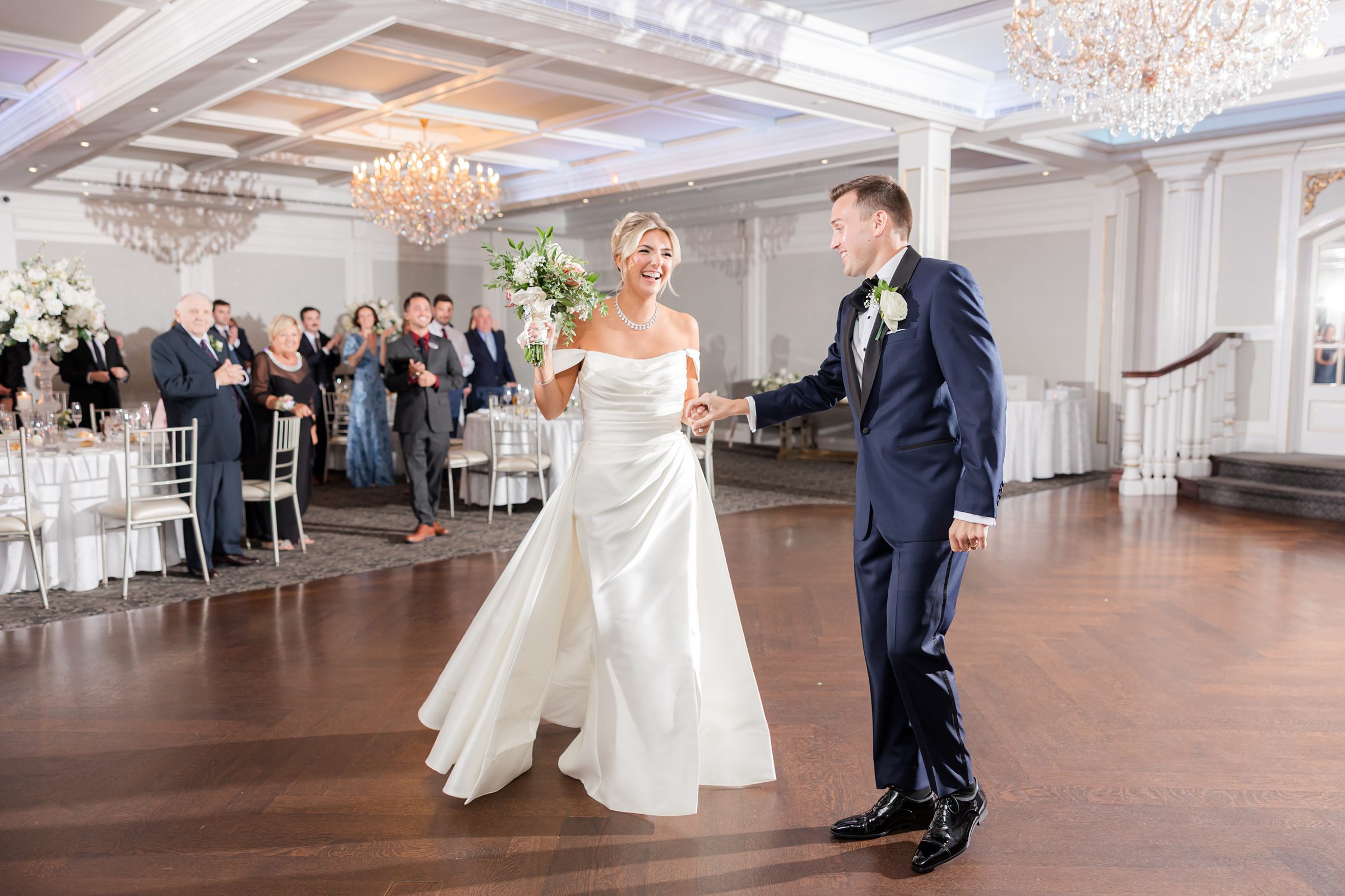 Bride twirls gracefully under the chandelier as her groom guides her, their laughter filling the room with warmth and romance.