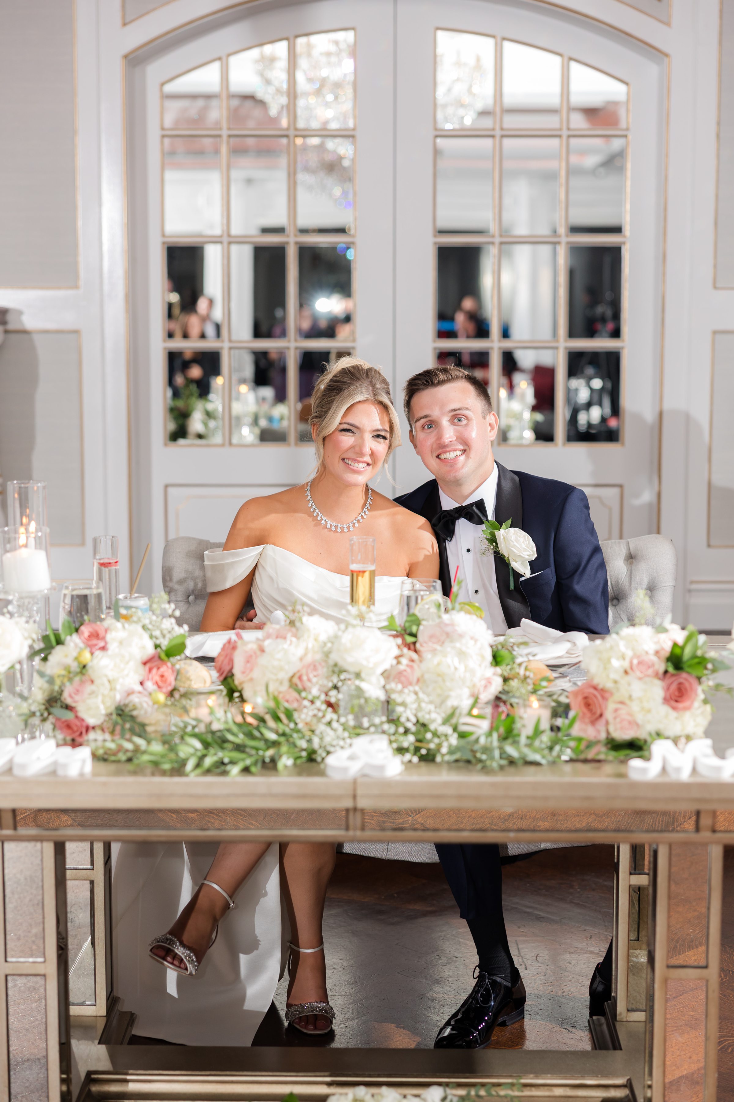 Seated together at their reception table, the couple leans into each other, glowing with happiness and love amid soft candlelight and florals.