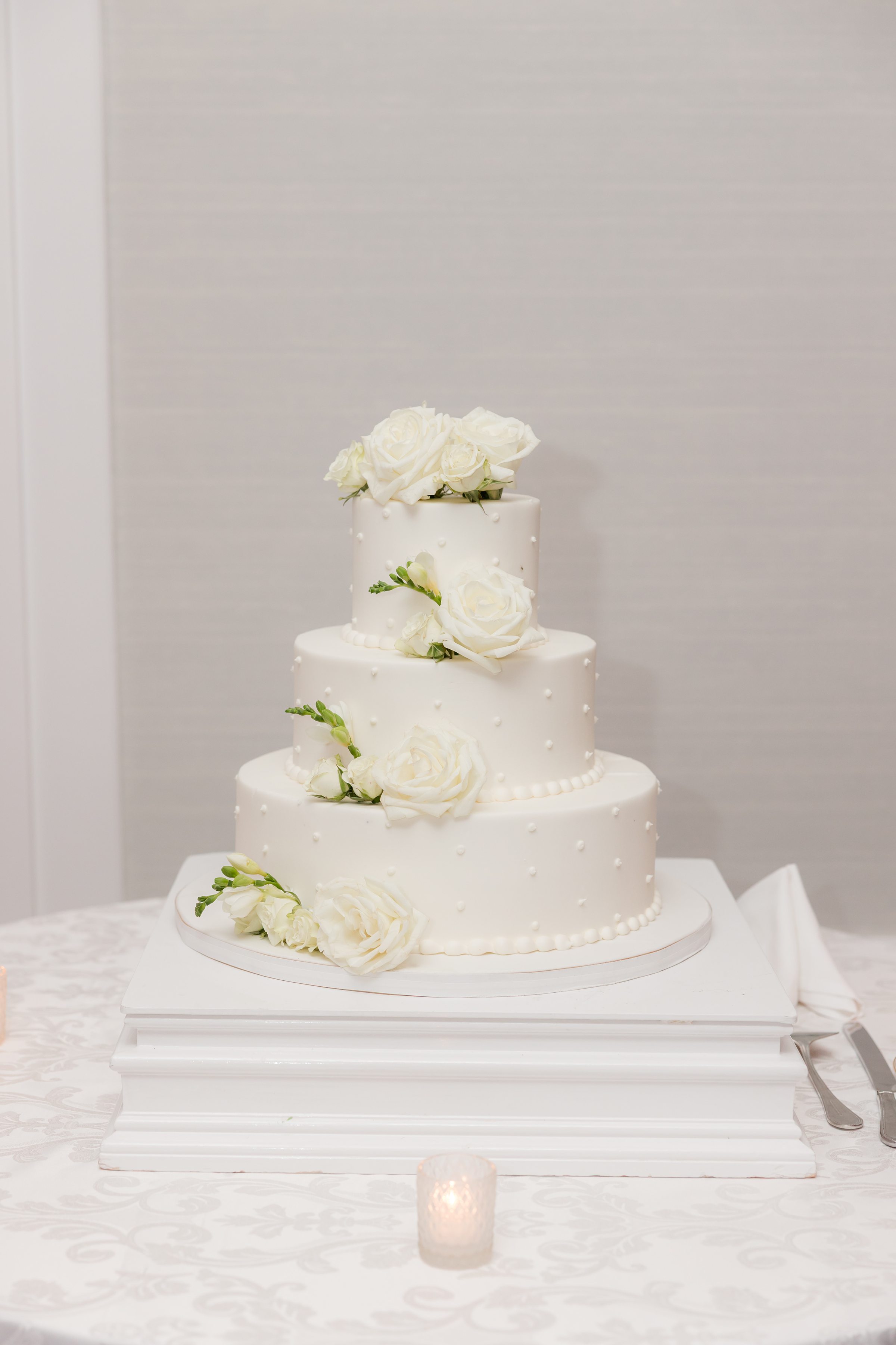 Delicate three-tier wedding cake adorned with white roses sits beautifully displayed, symbolizing the couple’s fresh and romantic beginning.