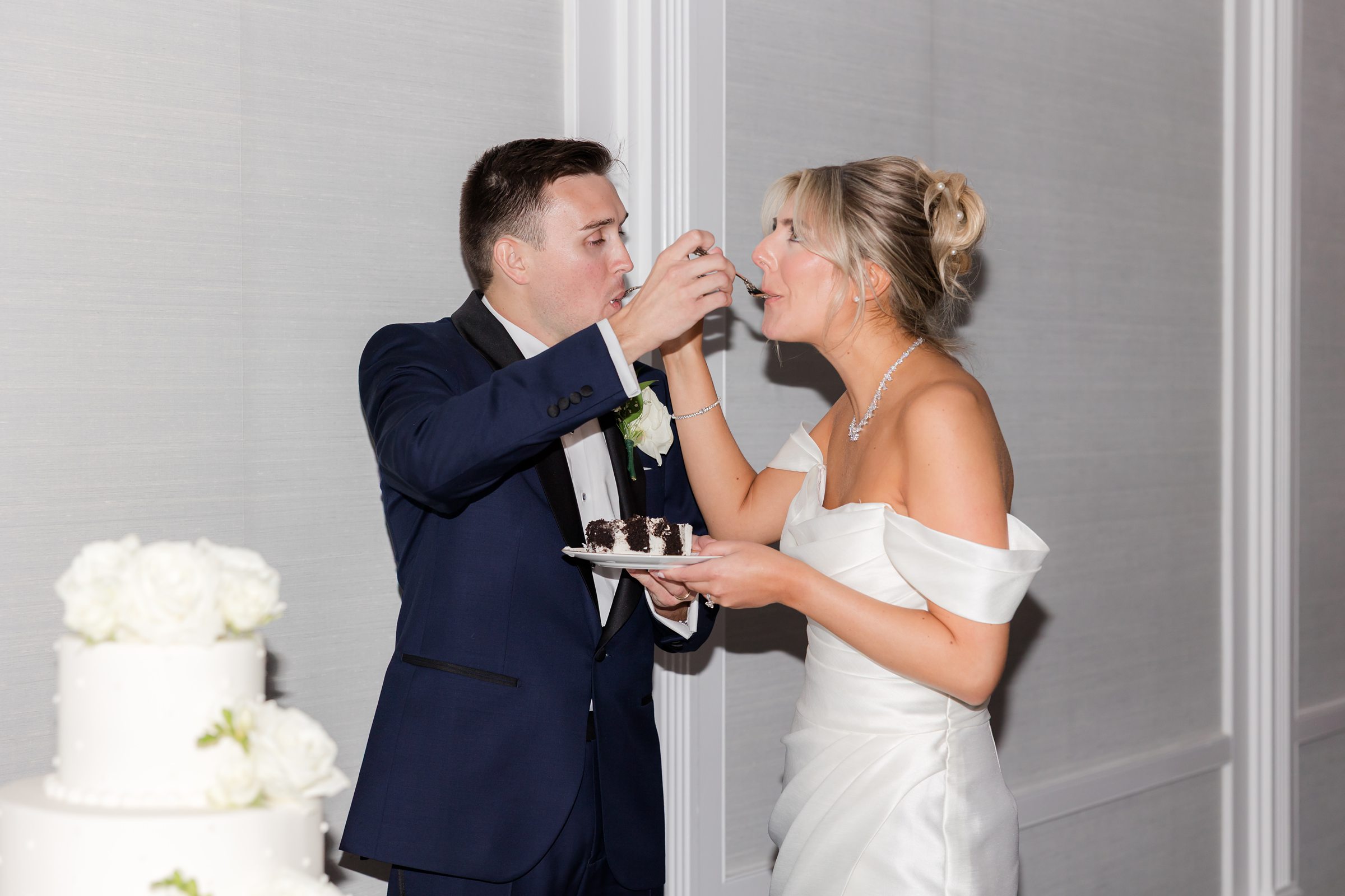 Bride and groom feed each other cake with laughter and tenderness, savoring a quiet, intimate moment together.