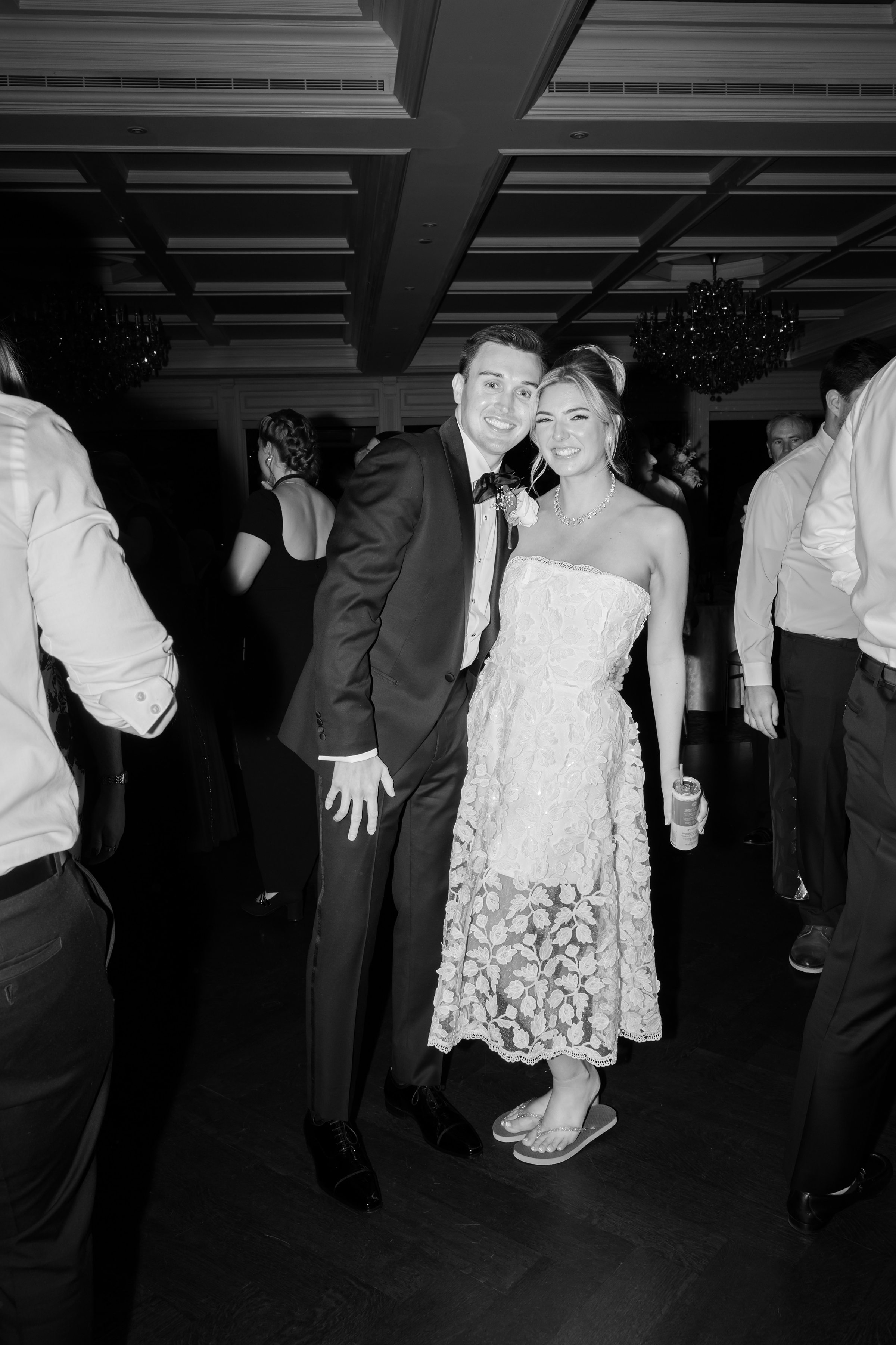 A joyful bride and groom lean into each other on the dance floor, smiling brightly as they celebrate their wedding night surrounded by loved ones.