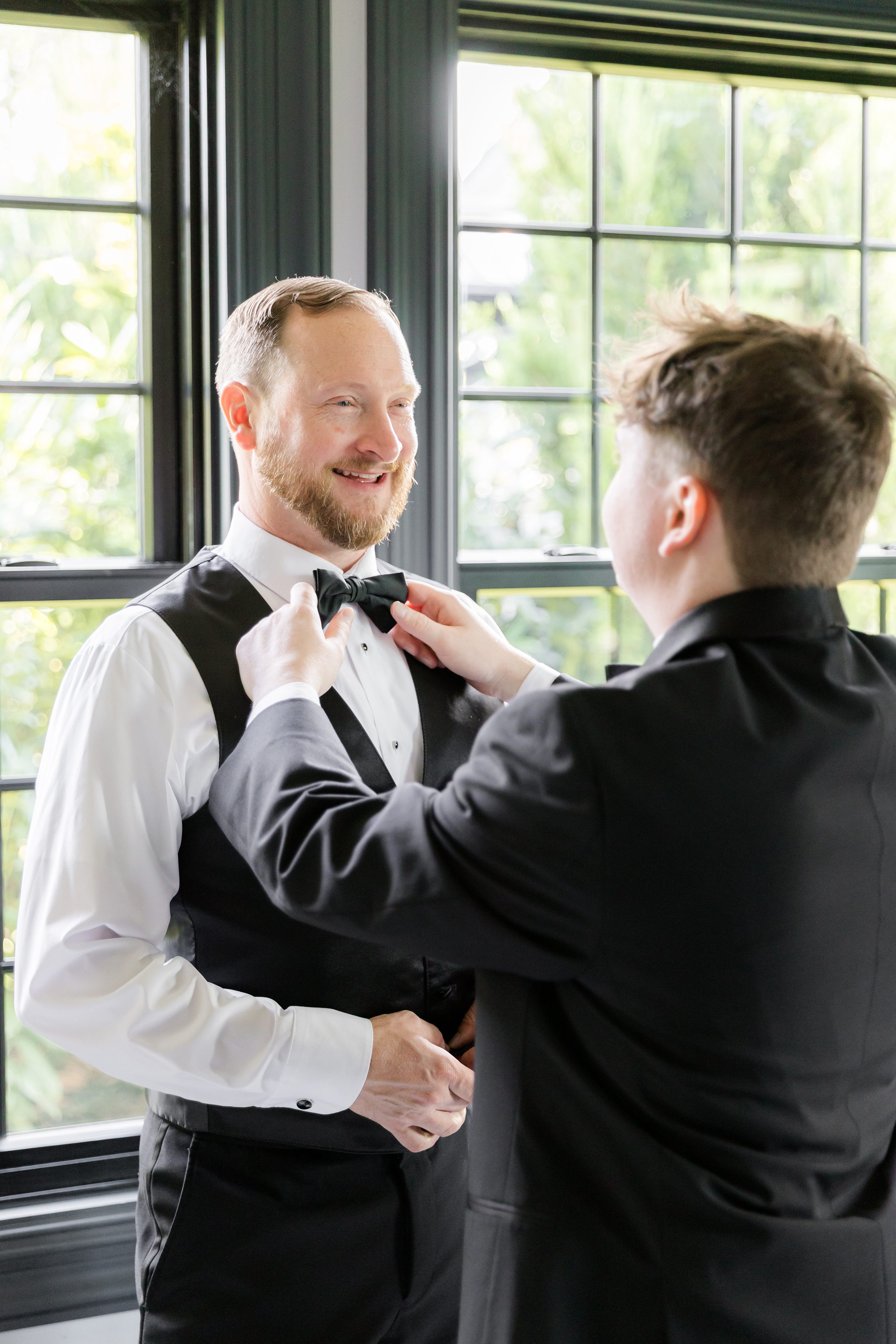 Groom’s bow tie is adjusted with care, a quiet moment of preparation and support