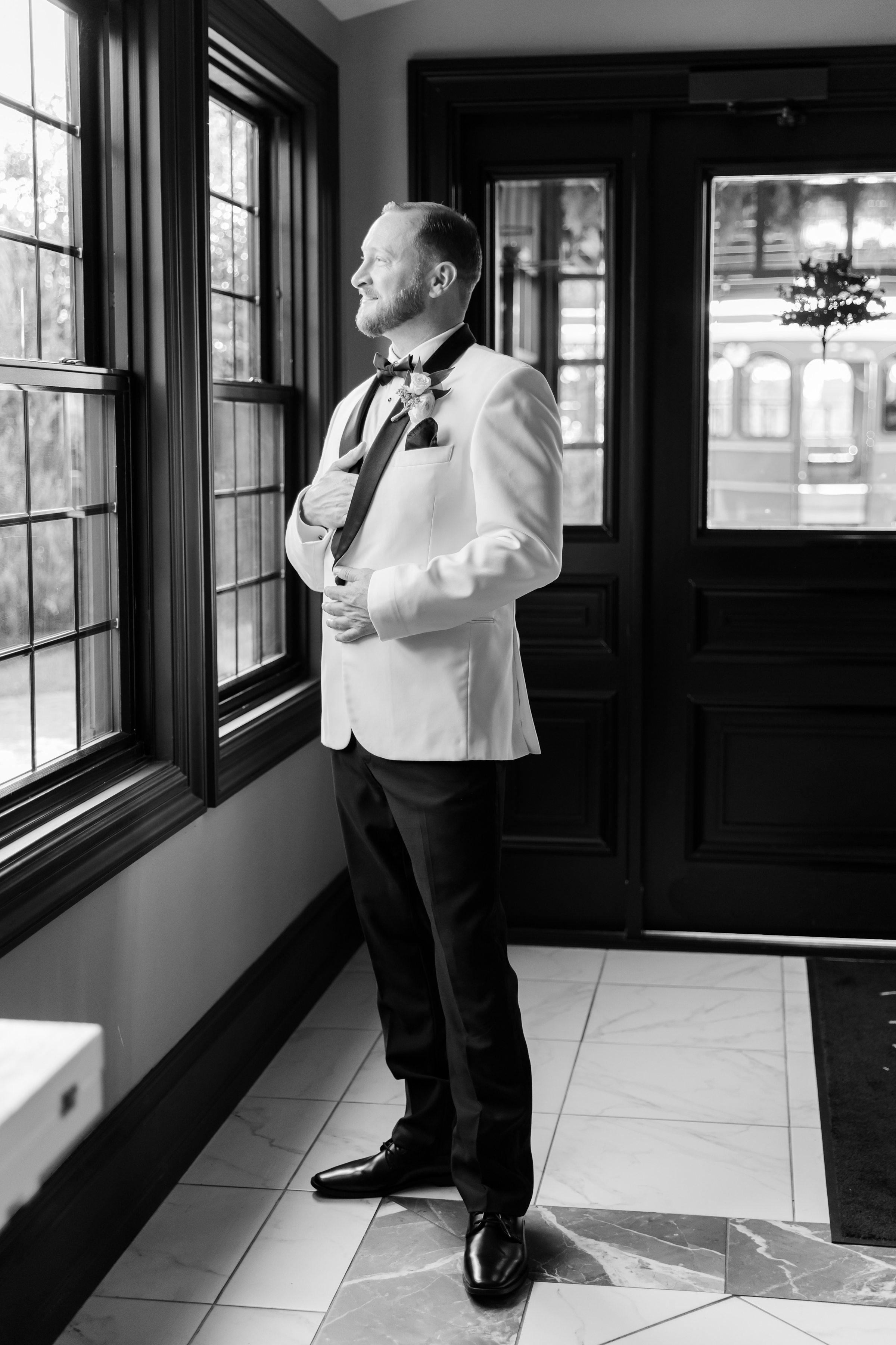 Groom stands by a window in soft light, reflecting before the ceremony
