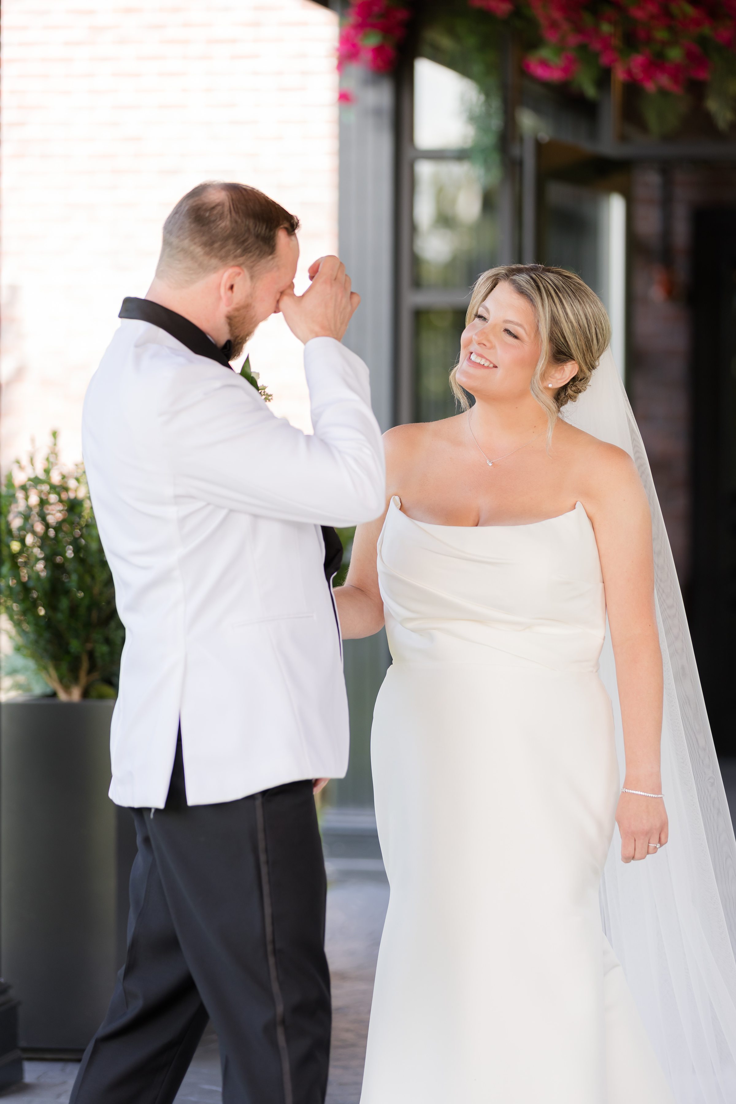 Groom wipes away tears as his bride looks on with tenderness and love.